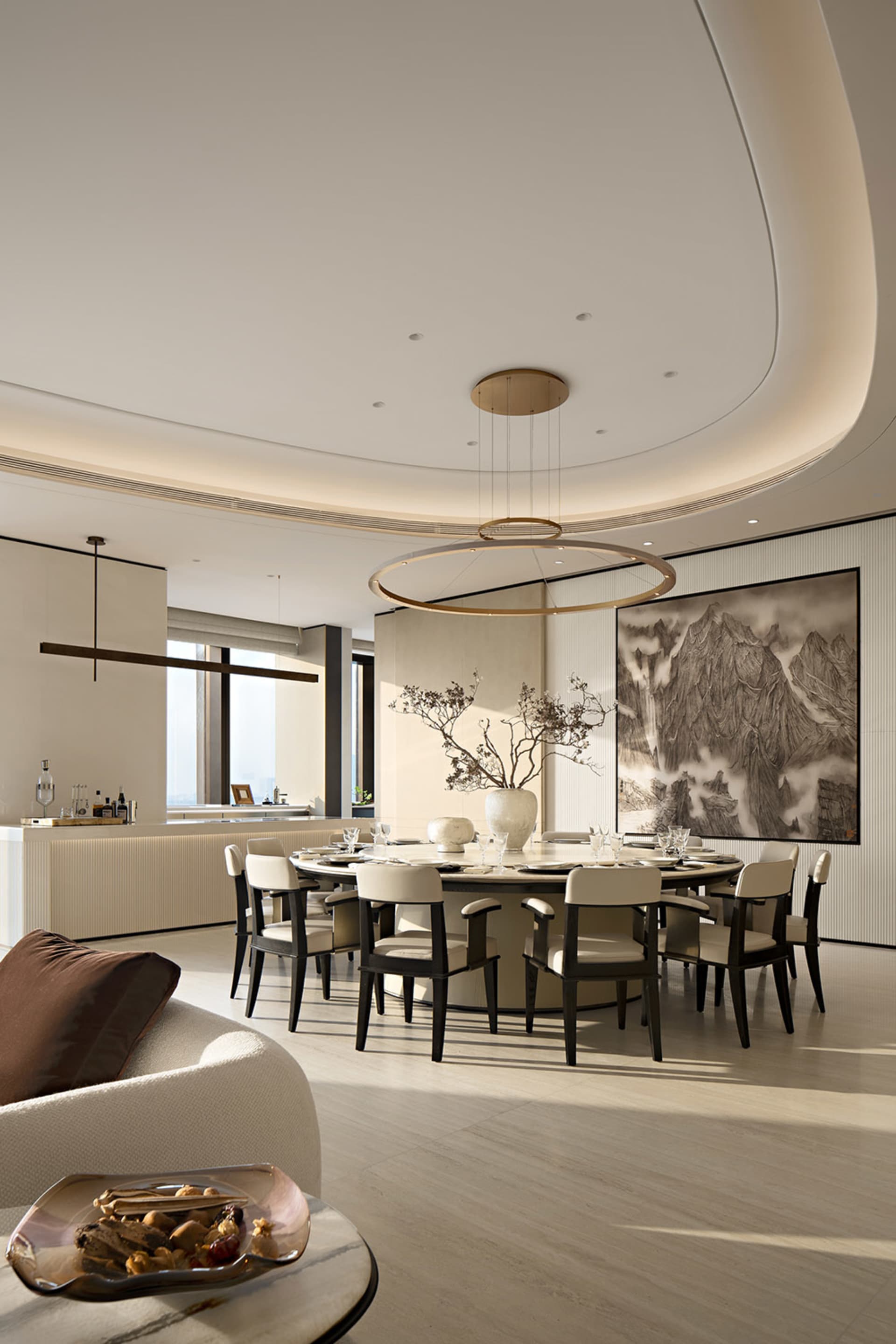 Modern luxury dining room featuring a large round walnut dining table with eight upholstered chairs, a dramatic circular pendant light, a large Chinese ink mountain painting, and a curved ceiling detail.