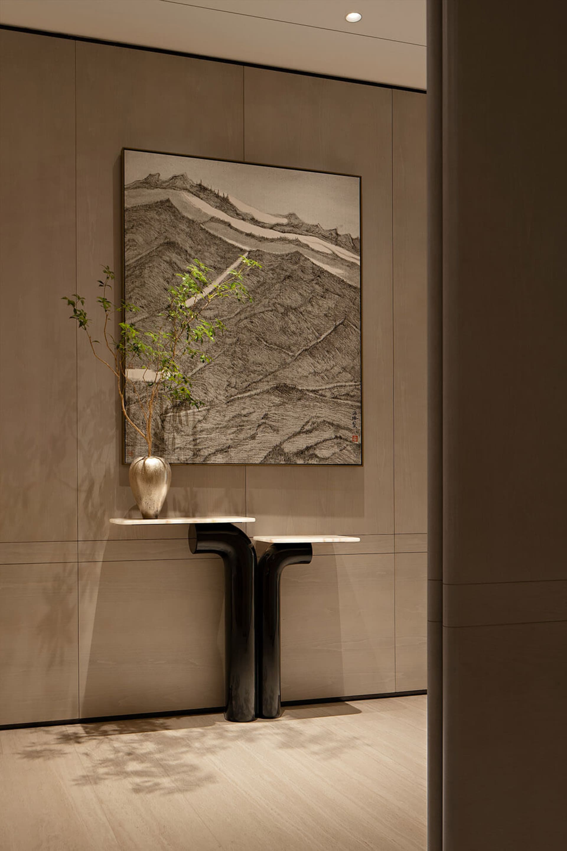 Modern minimalist entryway featuring a sculptural black console table, white marble top, metallic vase with greenery, and a large framed Chinese ink mountain painting against warm walnut paneling.