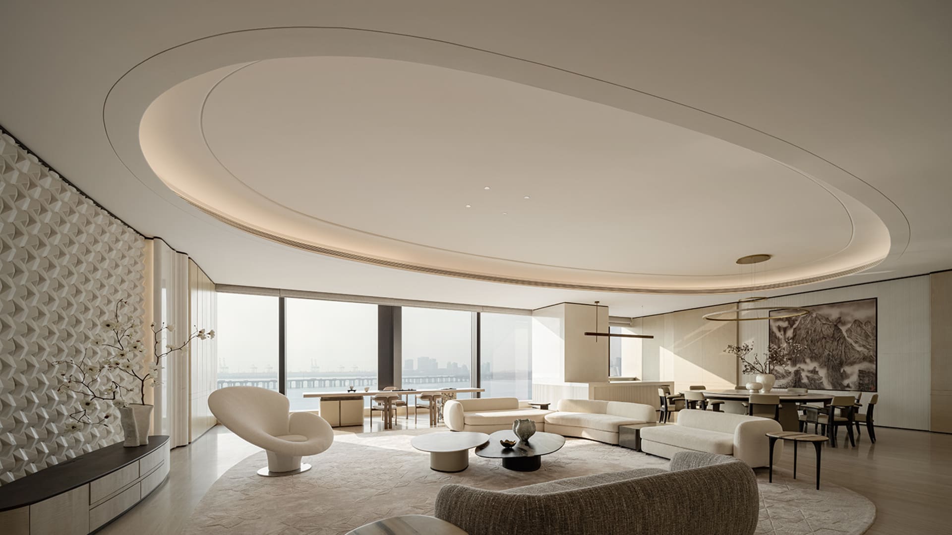 Modern luxury living room featuring a dramatic curved cove ceiling, textured white wall art, cream modular sofas, and large floor-to-ceiling windows with harbor view.
