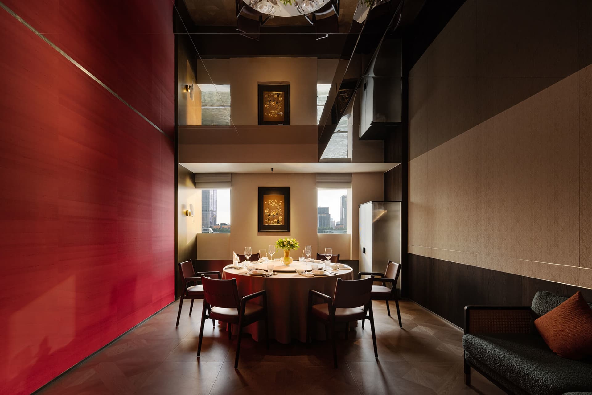 Modern private dining room featuring a bold red lacquer wall, round dining table with six chairs, double-height ceiling, and dark wood accents.