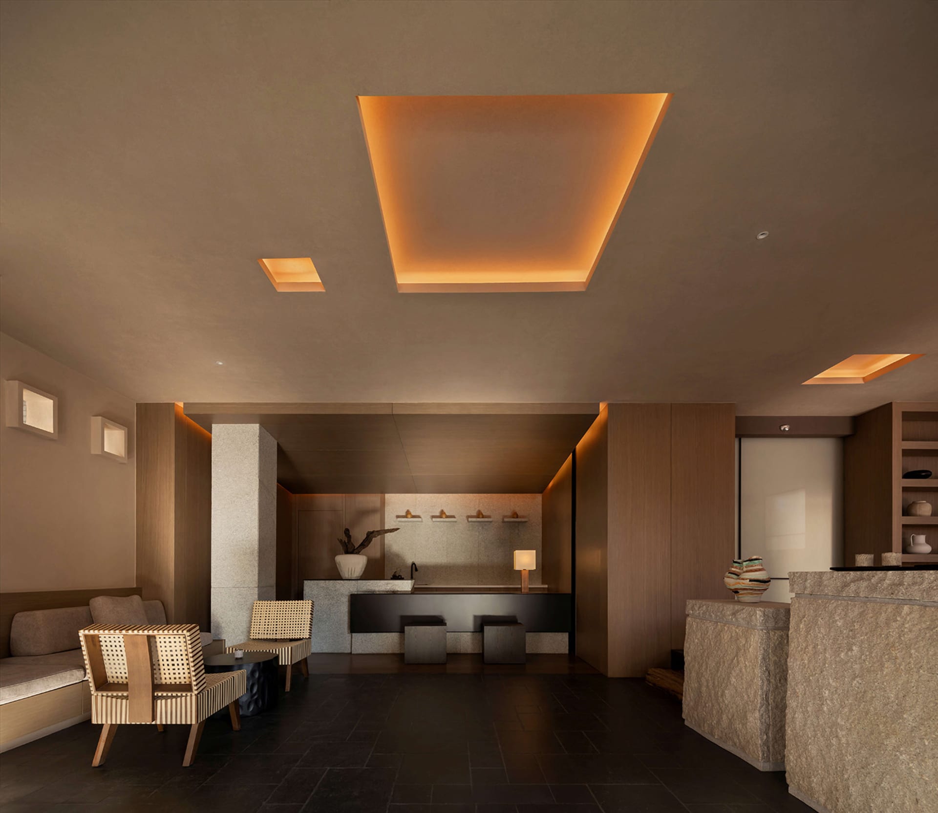 Modern minimalist hotel lobby featuring large travertine stone reception desk, woven rattan armchairs, dark tiled floor, and a dramatic square recessed ceiling with warm orange cove lighting.