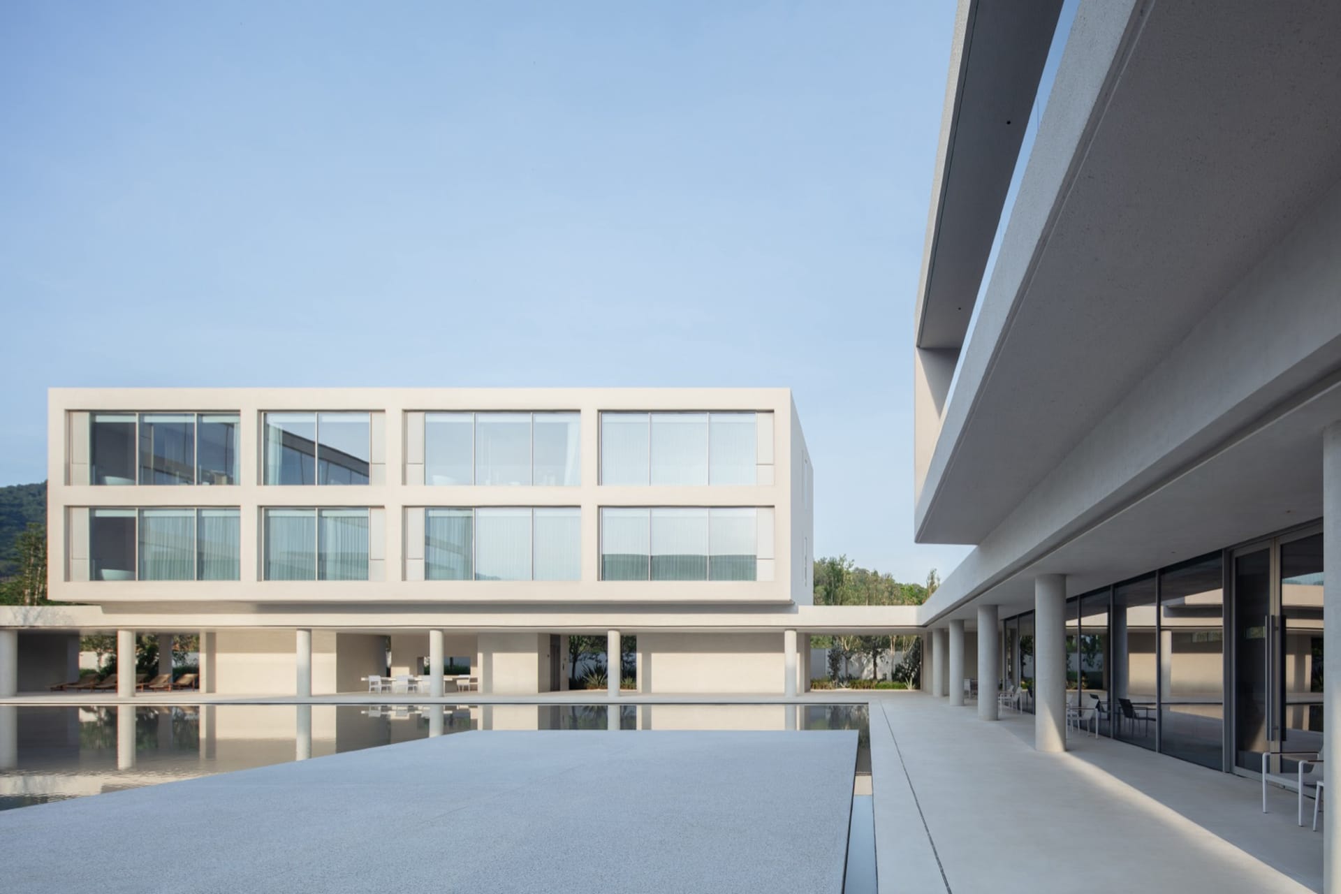 Modern minimalist concrete house with large reflecting pool in a central courtyard, featuring floor-to-ceiling windows and covered outdoor walkways.