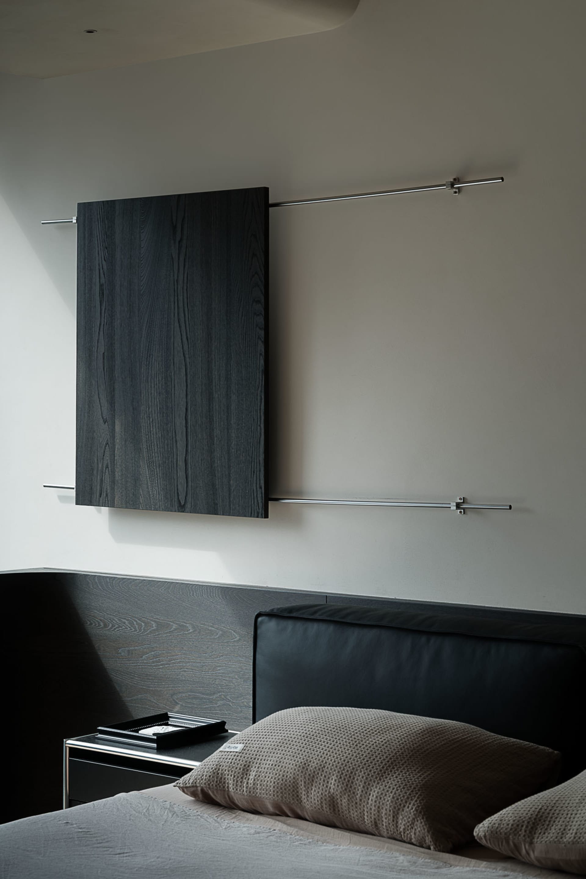 Modern minimalist bedroom featuring a black oak floating headboard and matching wall-mounted console, paired with a black leather headboard and neutral textured pillows.