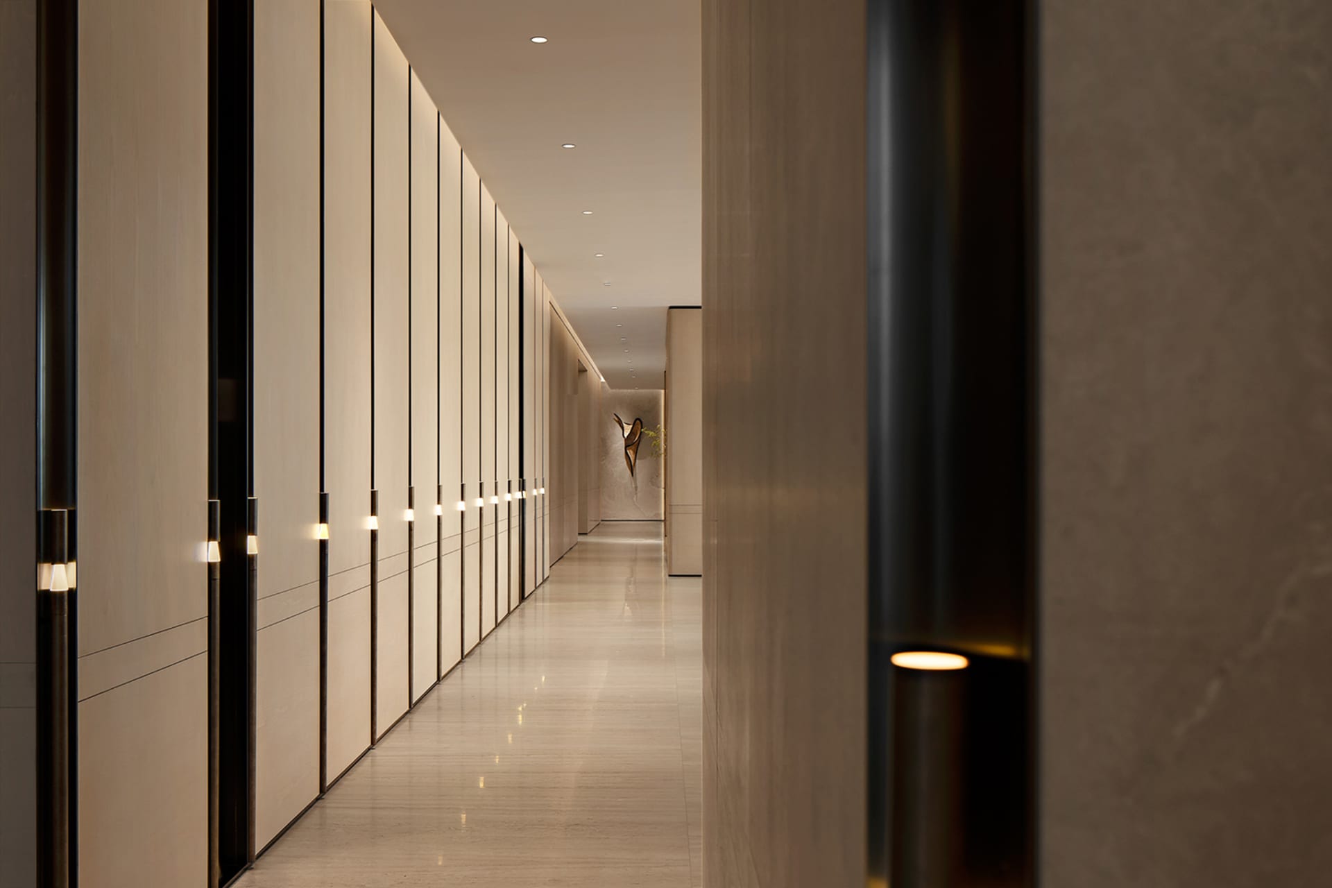 Long modern hallway featuring floor-to-ceiling light wood paneling with integrated vertical LED lighting and polished stone flooring.