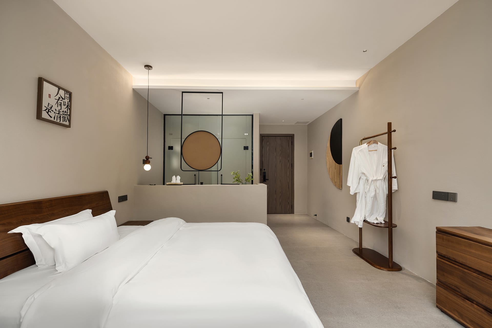 Modern minimalist hotel bedroom with walnut wood headboard, white bedding, pendant light, and circular wall art in neutral tones.