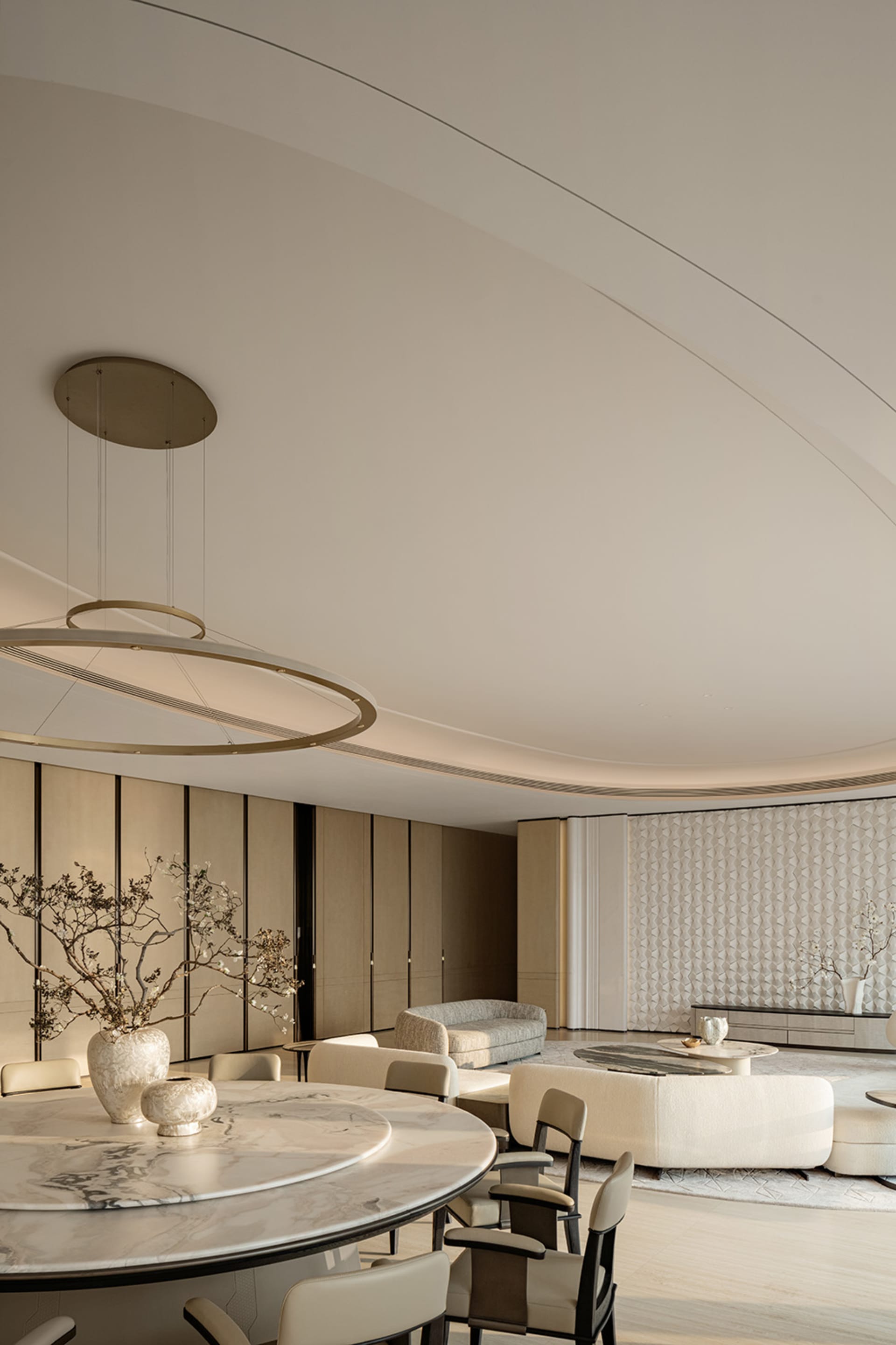 Modern luxury open-plan living and dining area featuring a large round white marble dining table, sculptural circular pendant light, curved ceiling, and neutral-toned contemporary furniture.