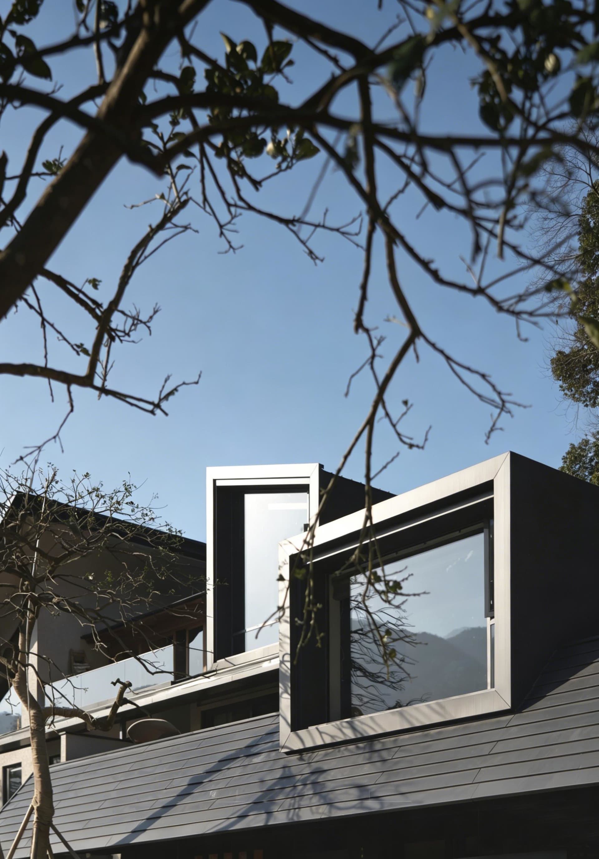 Low-angle view of a contemporary mountain residence featuring dark metal cladding, large picture windows, and dramatic geometric forms against a clear blue sky, partially framed by tree branches.