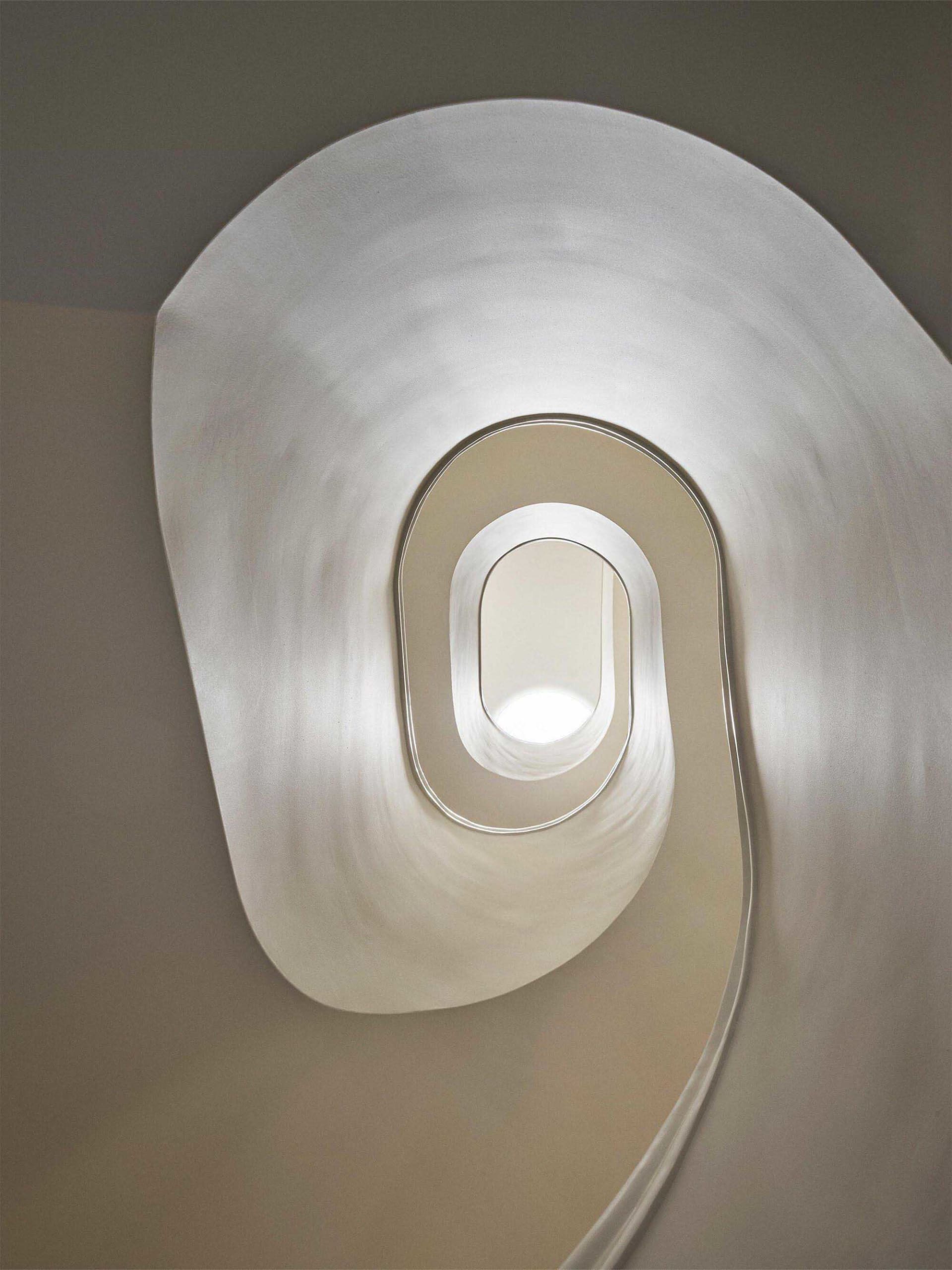 View looking down into a sculptural white spiral staircase with smooth organic curves and integrated lighting.