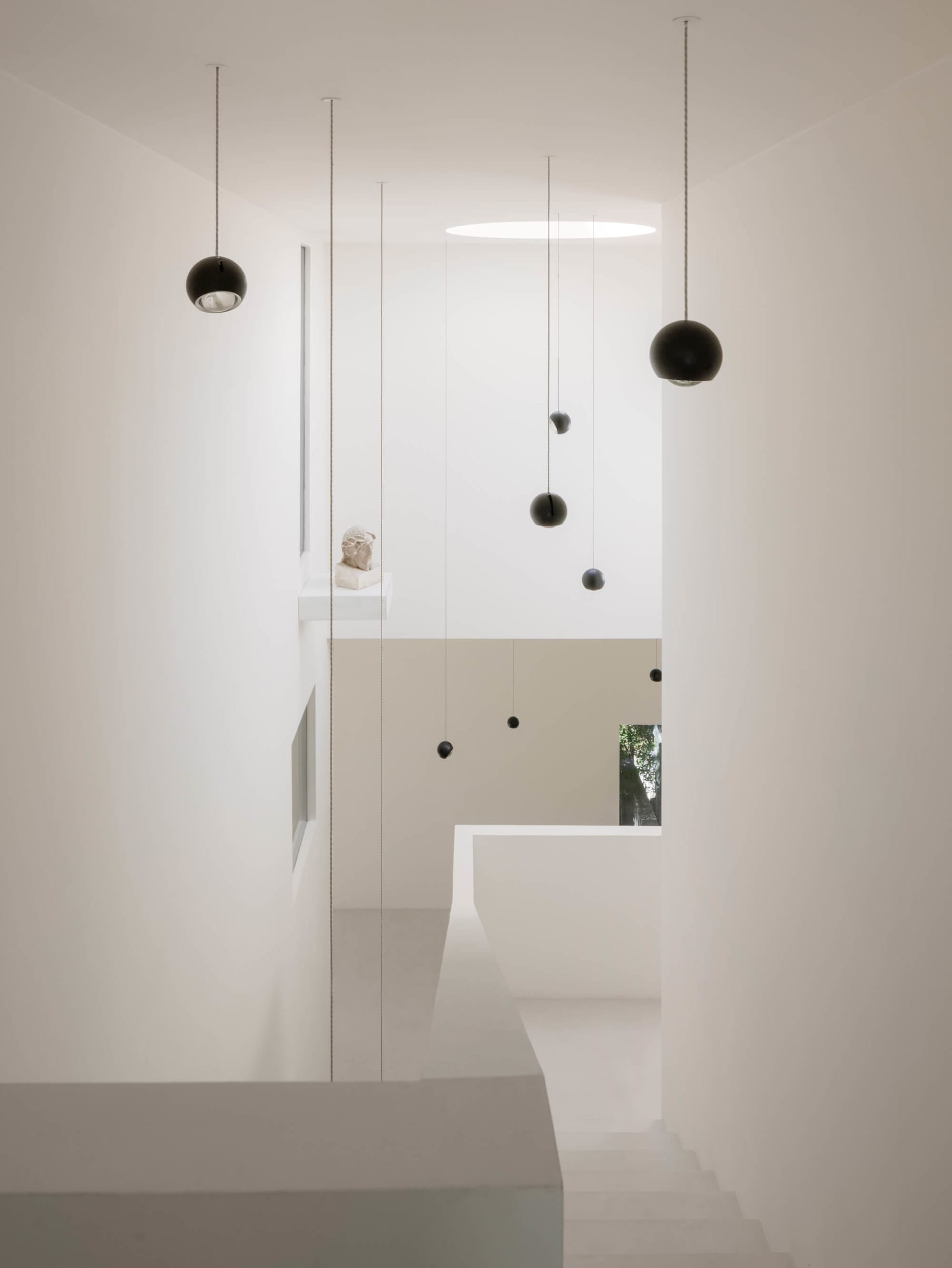 Modern minimalist double-height staircase with white plaster walls and multiple black spherical pendant lights hanging at different heights.