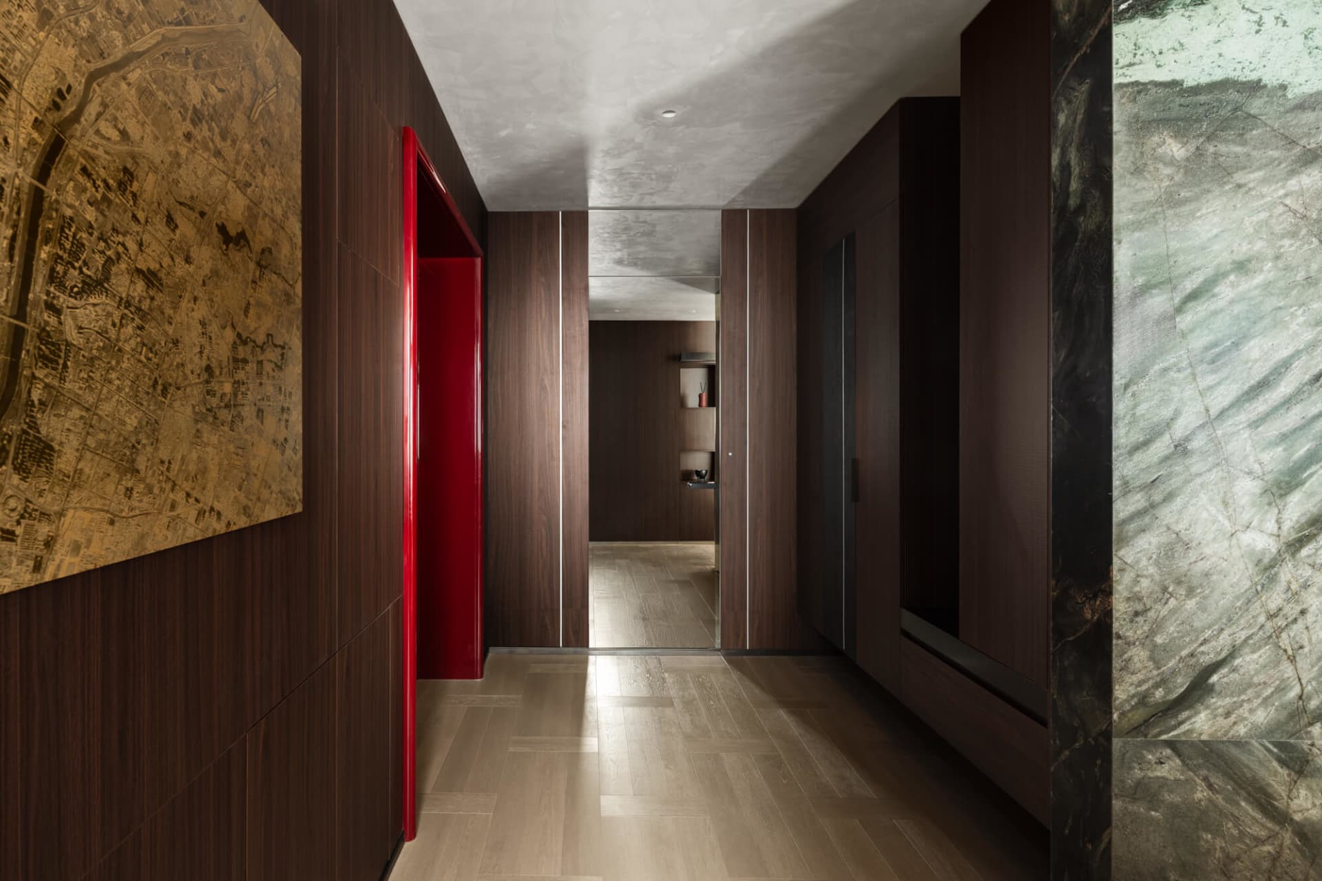 Modern luxury hallway with dark walnut wood walls, a glossy red door, green marble feature wall, and large city map artwork.