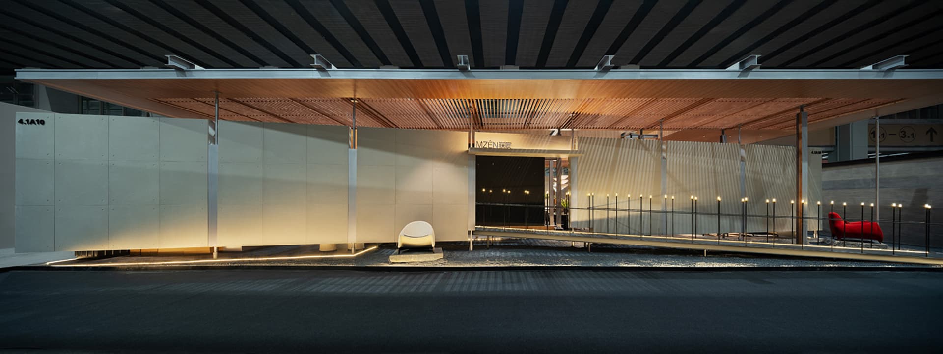 Modern airport lounge interior at night with a large wooden slatted canopy, linear LED lighting, white concrete walls, and red and white sculptural seating.