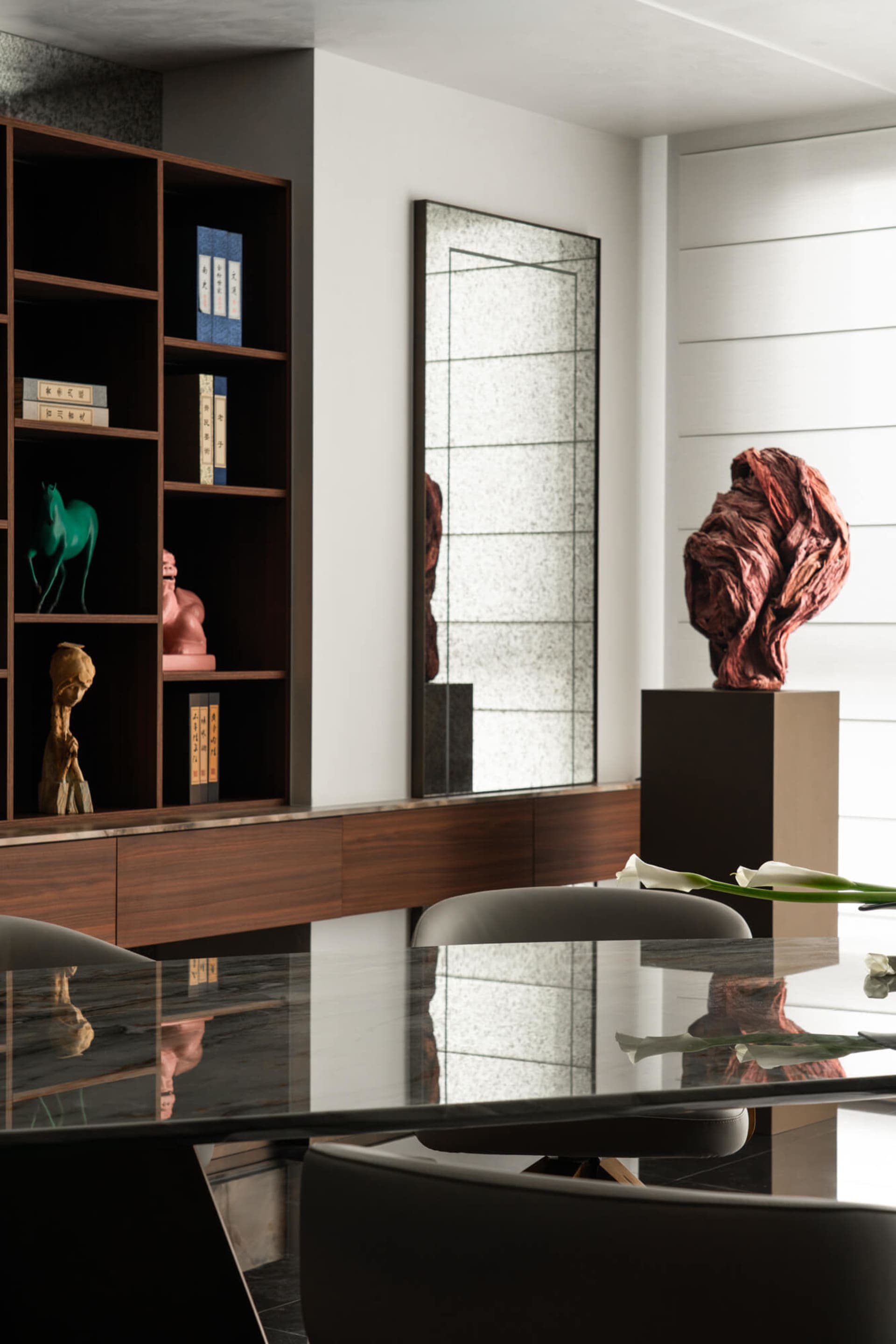 Modern dining room featuring a dark walnut built-in cabinet displaying Chinese art pieces, a large textured mirror, and a dramatic red stone sculpture on a pedestal, with a glossy black dining table in the foreground.
