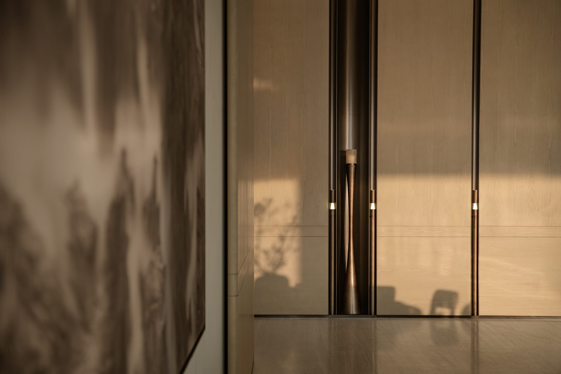 Modern minimalist entryway featuring light wood cabinetry with vertical warm LED lighting strips and a large abstract painting on the left wall.