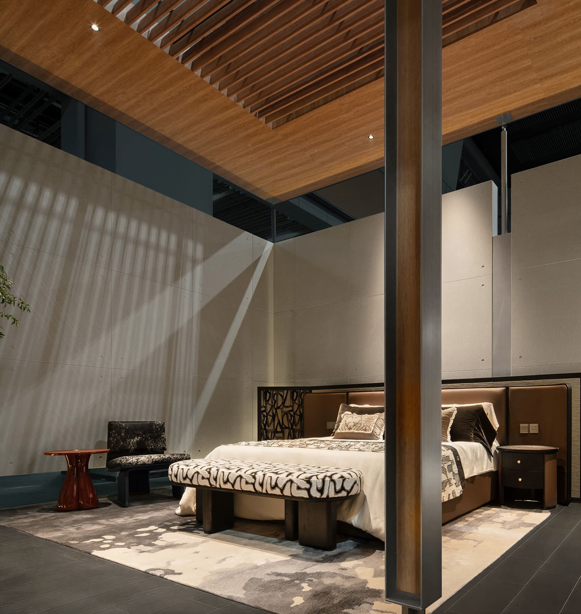 Modern luxury bedroom featuring a walnut slatted ceiling, concrete accent wall with dramatic sunlight shadows, upholstered bed with patterned bench, and layered neutral textiles.