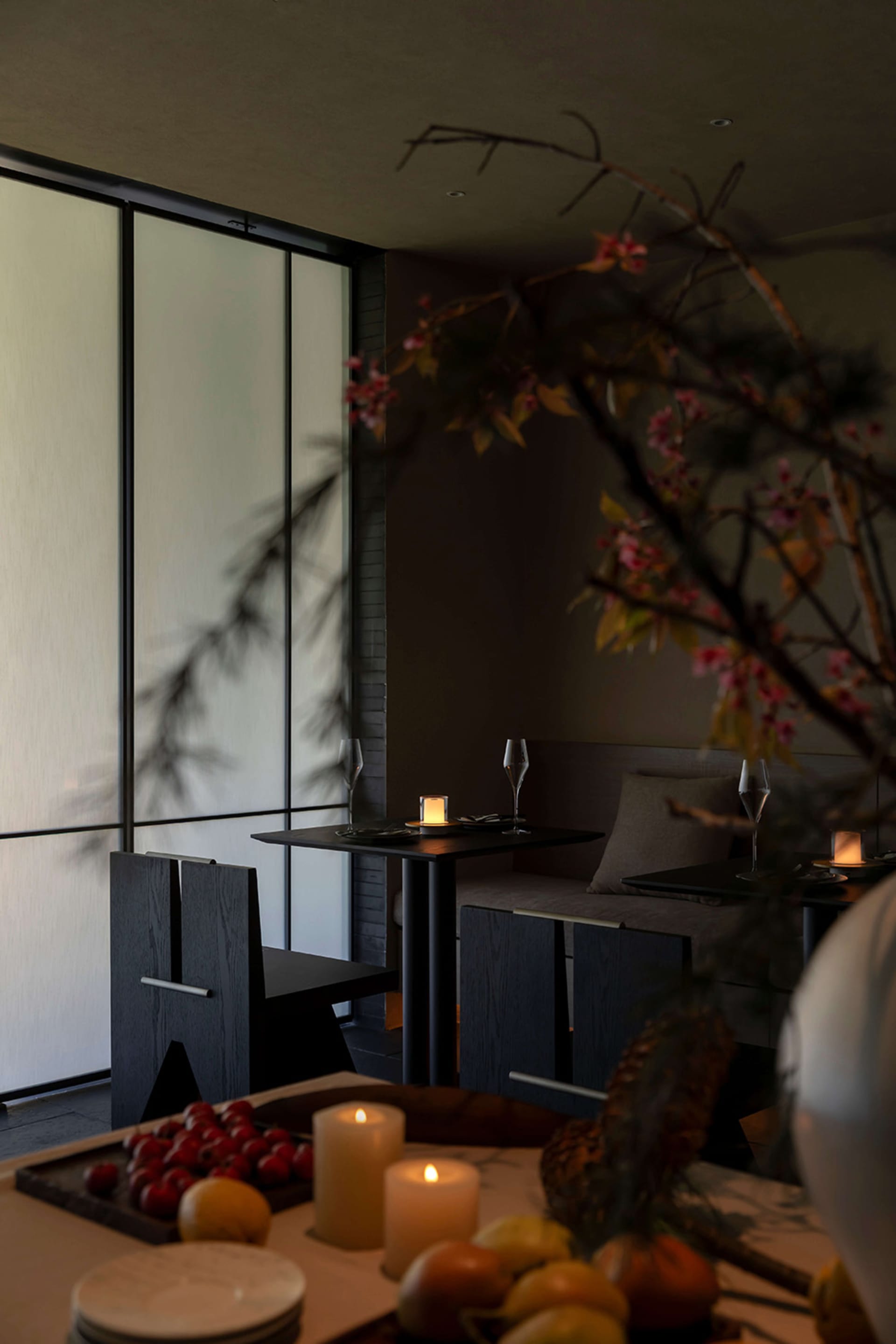 Modern dark oak dining room featuring built-in banquette seating, black dining table, and glowing candles with large windows in the background.