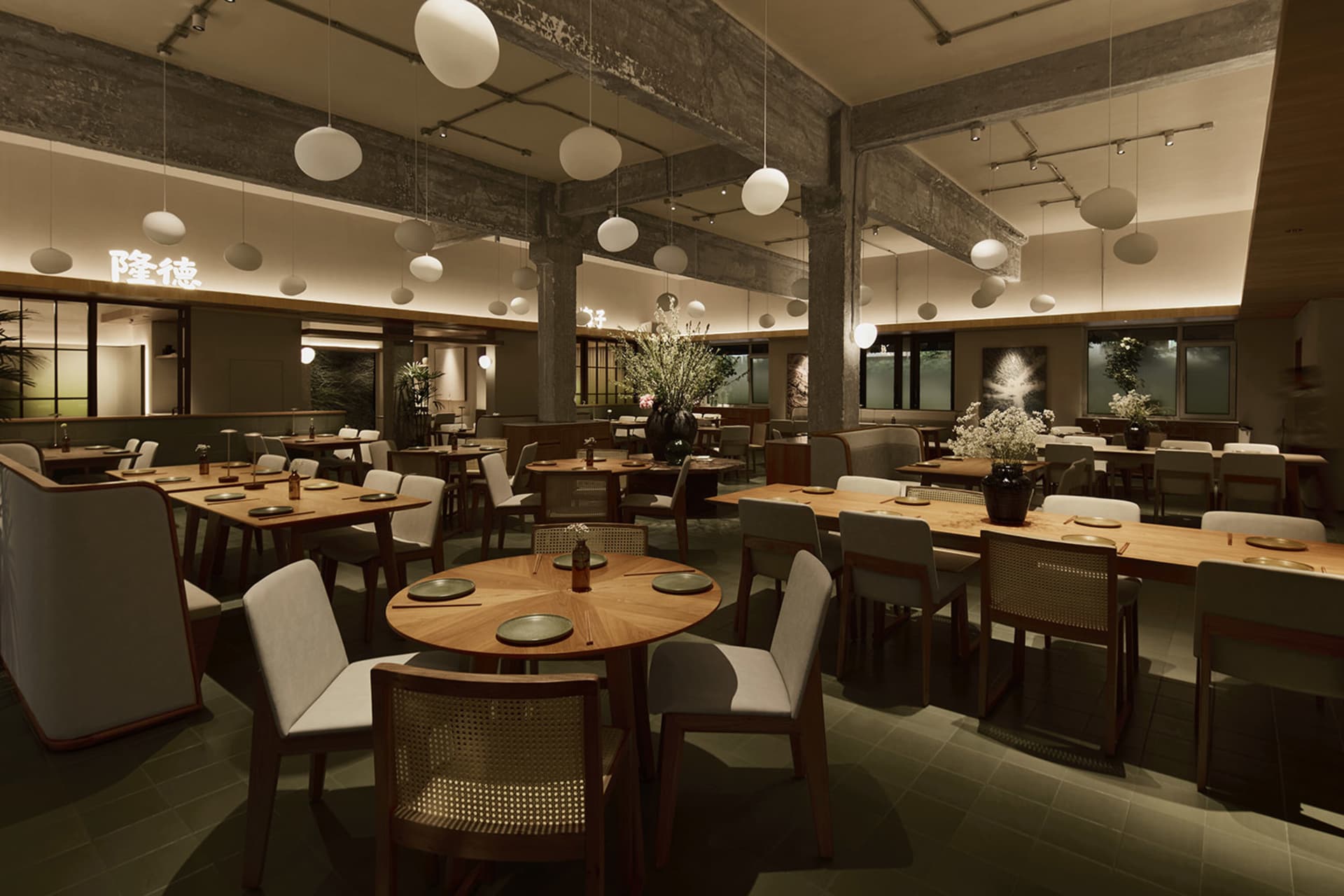 Modern industrial-style restaurant interior featuring wooden dining tables, woven rattan chairs, exposed concrete beams, and numerous spherical pendant lights.