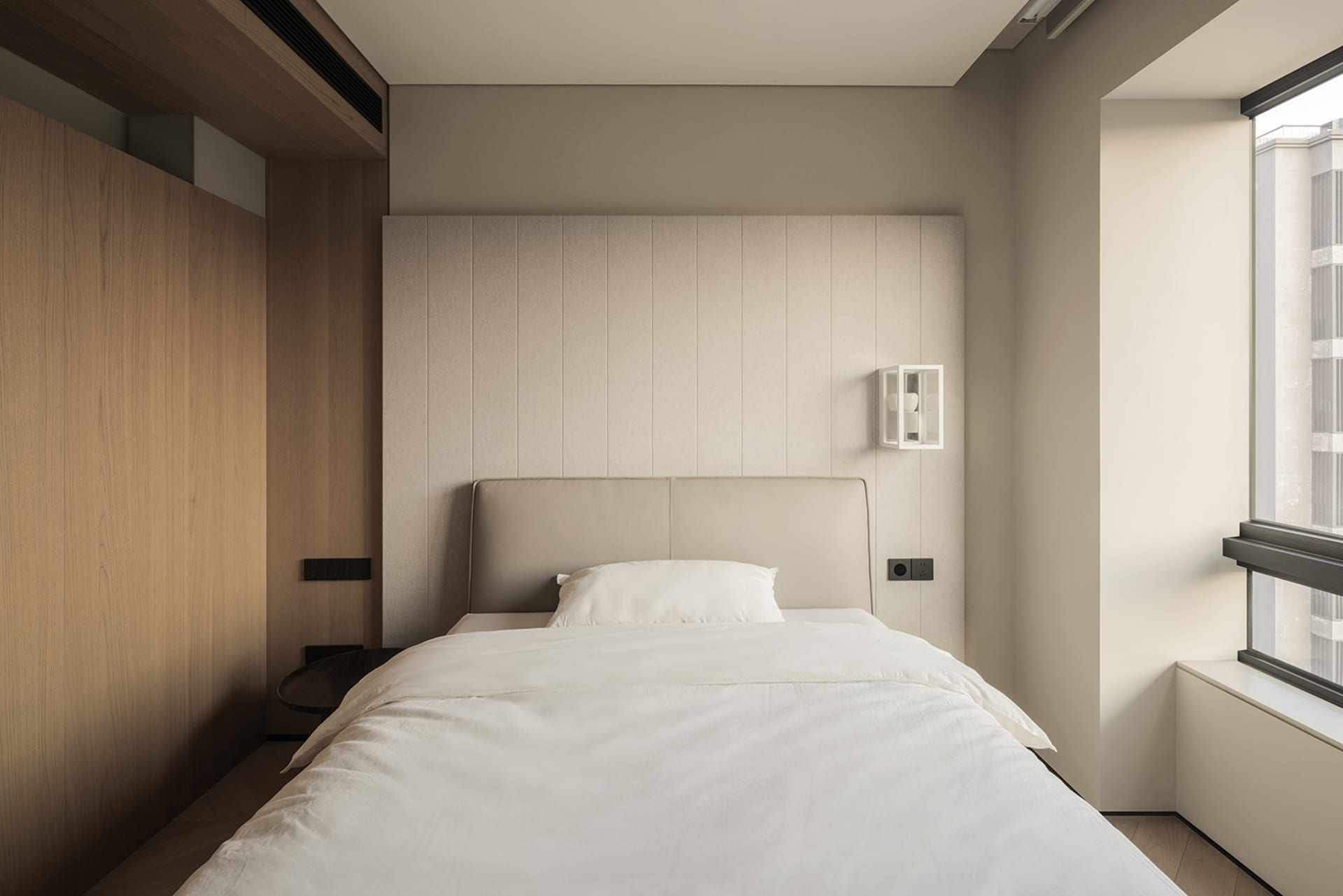 Modern minimalist bedroom with a beige upholstered bed, white linens, vertical wood panel accent wall, and large window with natural light.