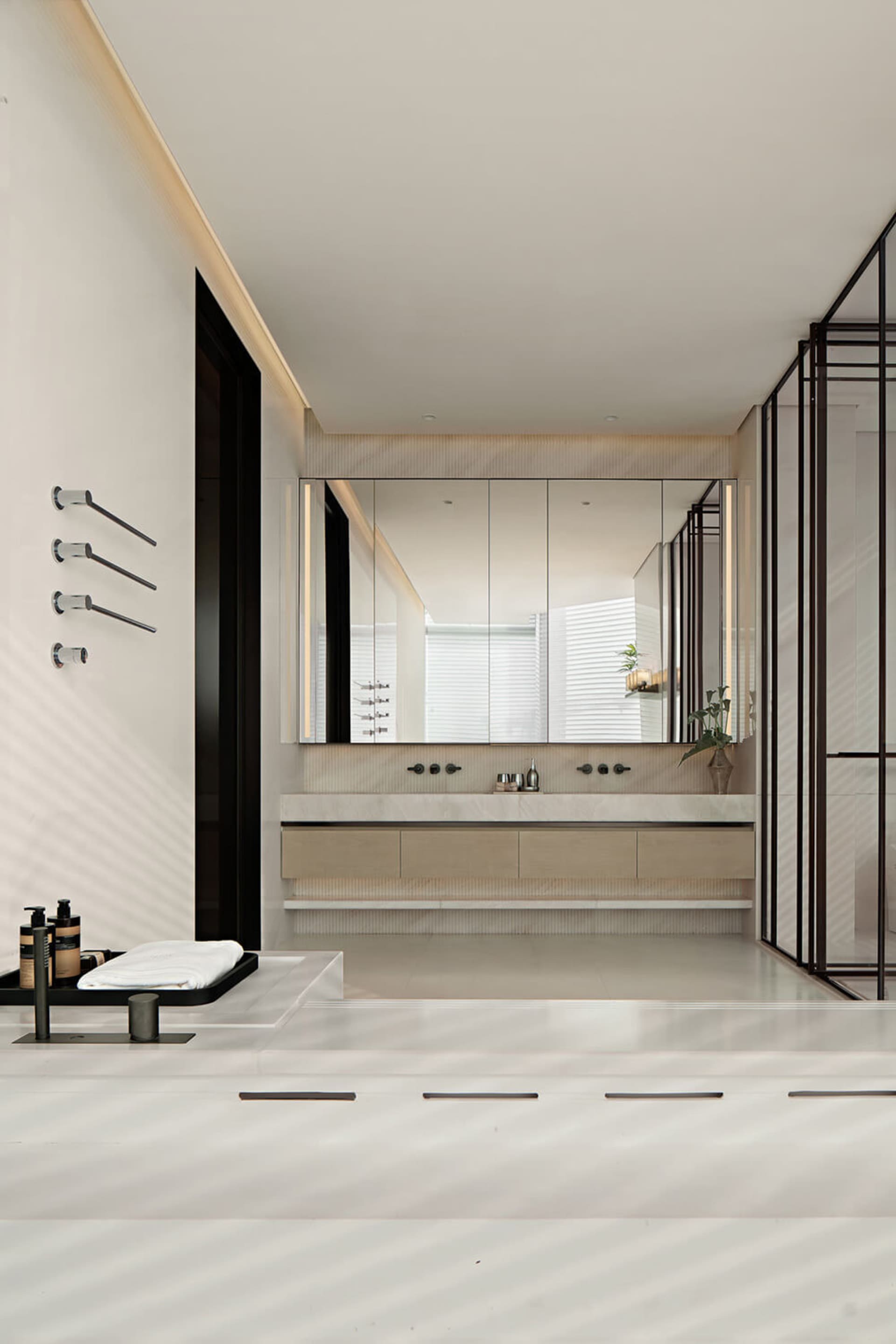 Modern minimalist bathroom with white marble surfaces, floating light-wood vanity, large backlit mirror, and black metal accents