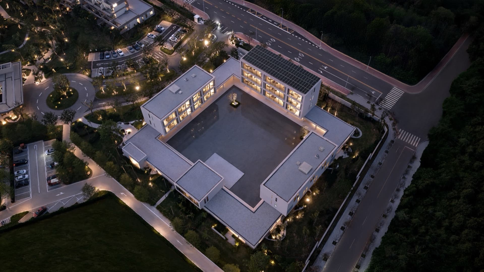 Aerial night view of a modern U-shaped concrete villa with a large central courtyard, surrounded by landscaped grounds and roads.