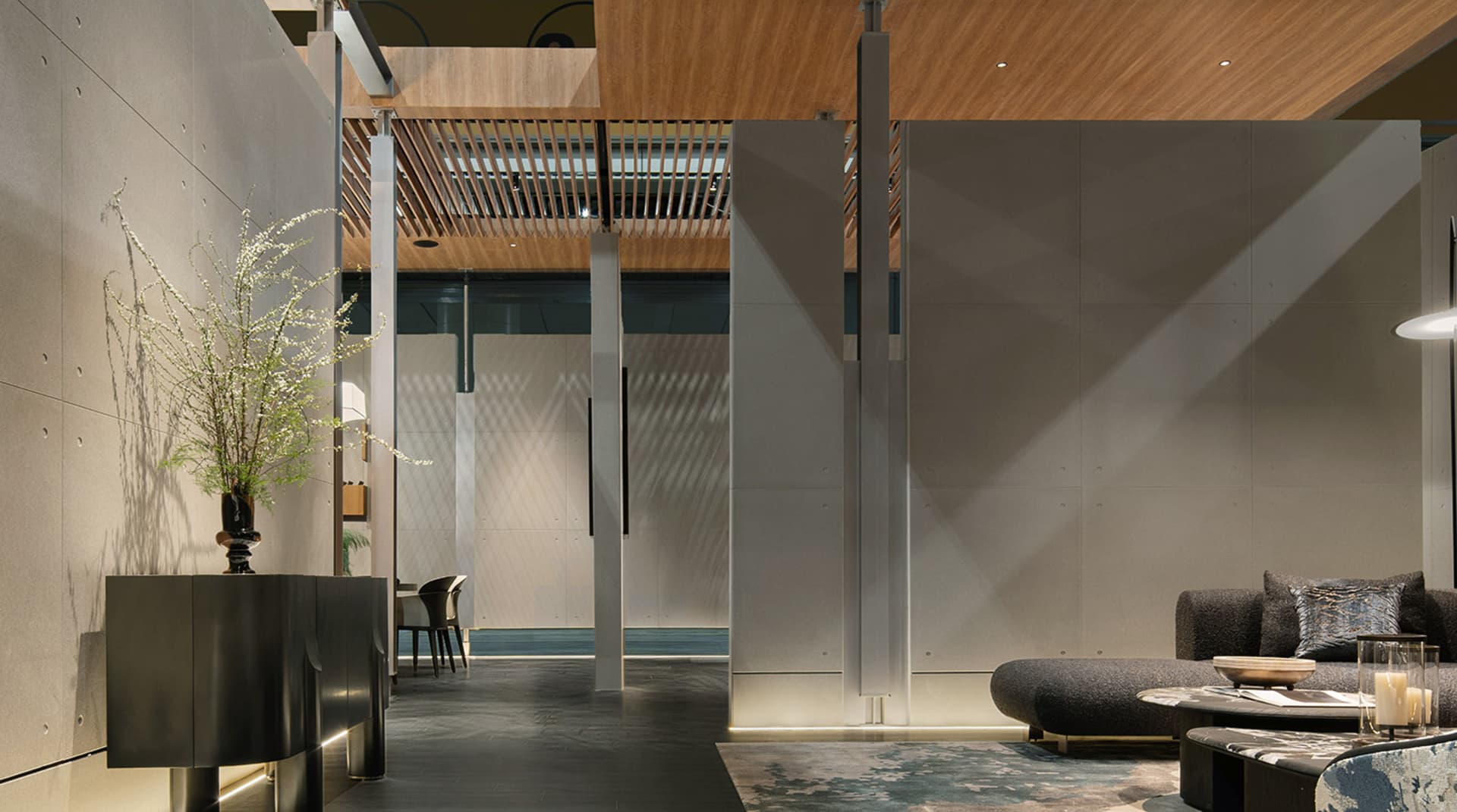 Modern minimalist living room featuring large concrete panels, warm wood slat ceiling, dark textured sofa, and sculptural floral arrangement on a black console.