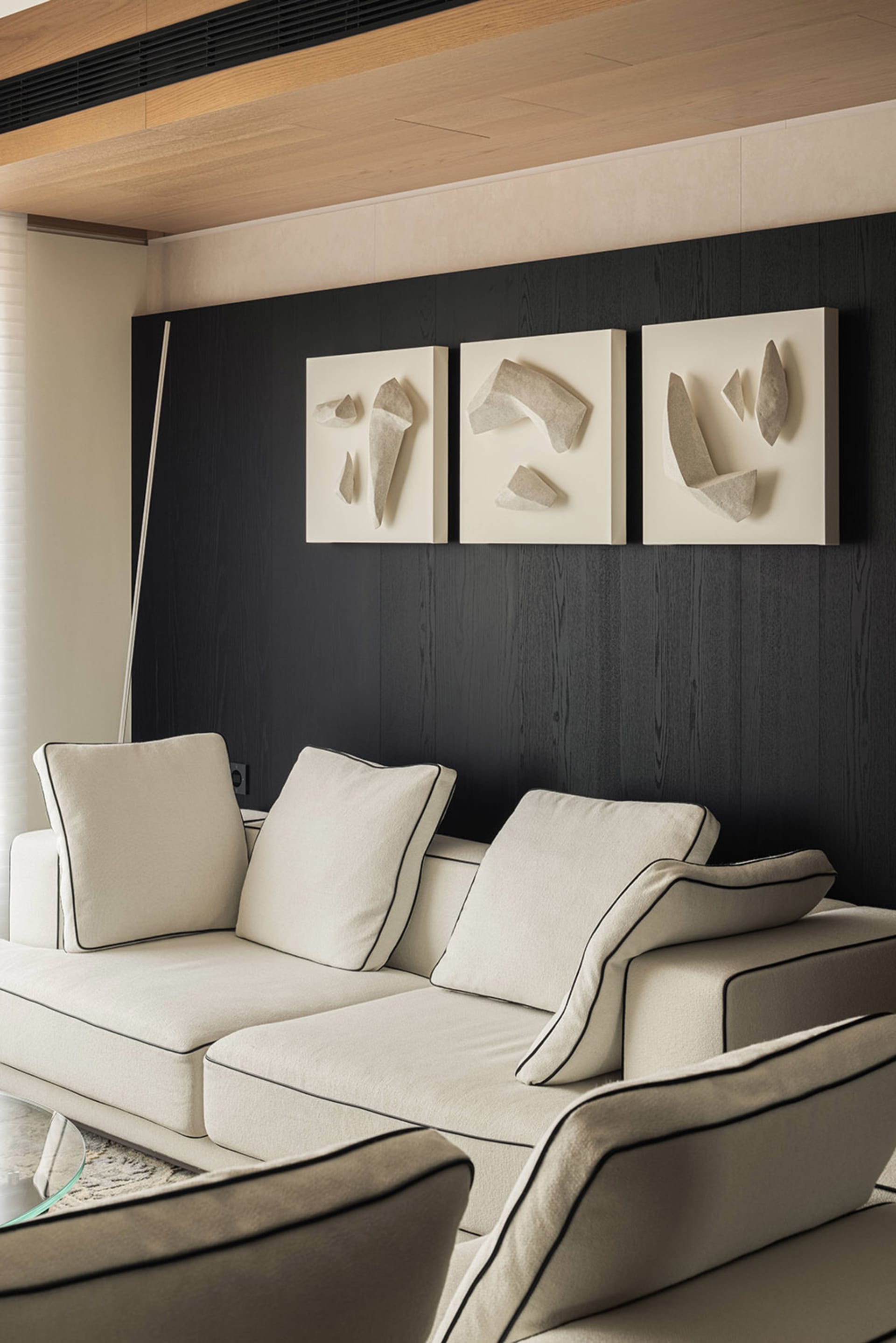 Modern living room with off-white sectional sofa, black wood accent wall, and three-piece textured beige wall art installation.