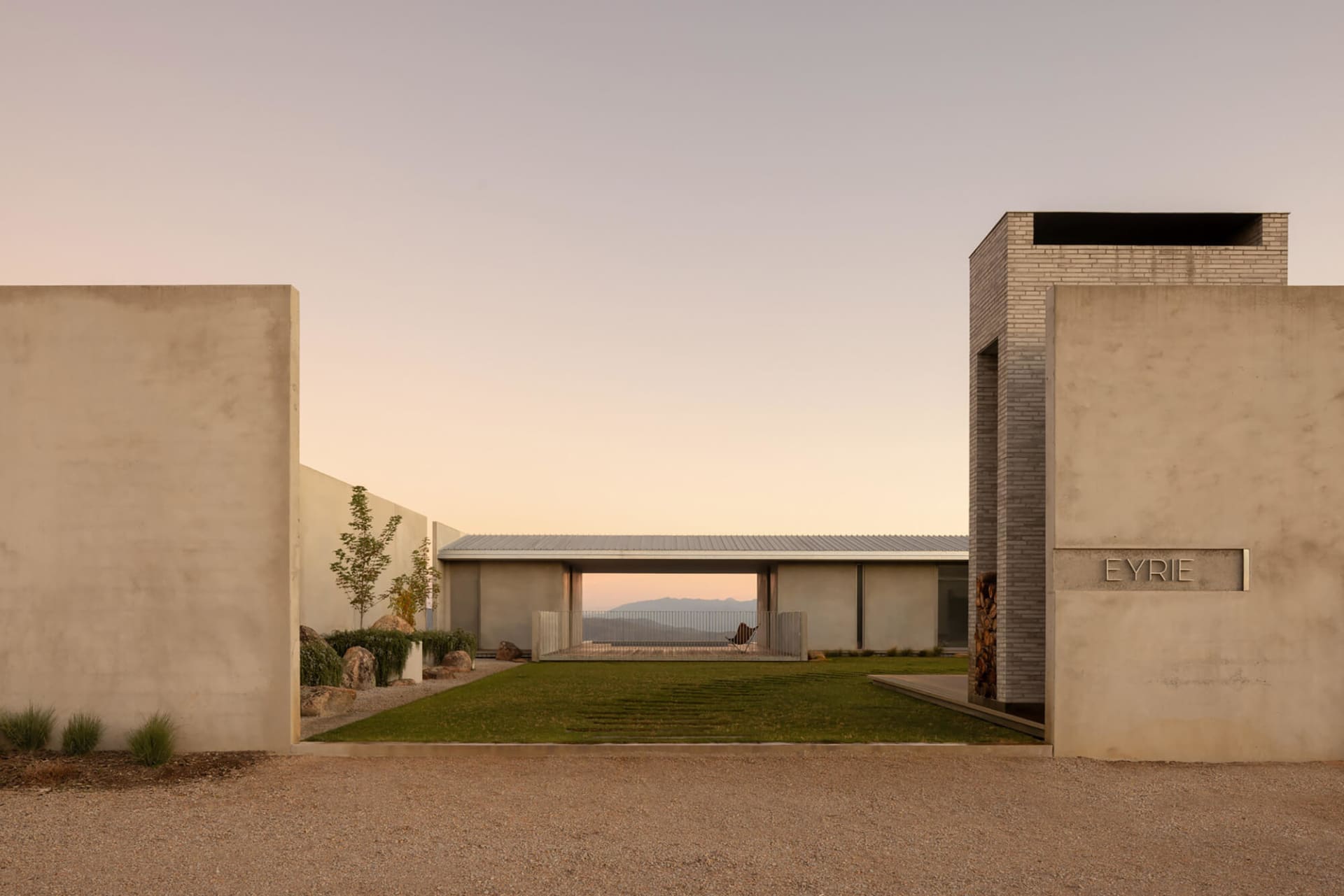 Modern concrete courtyard house named Eyrie with a perfectly manicured lawn, minimalist walls, and a mountain view at sunset.
