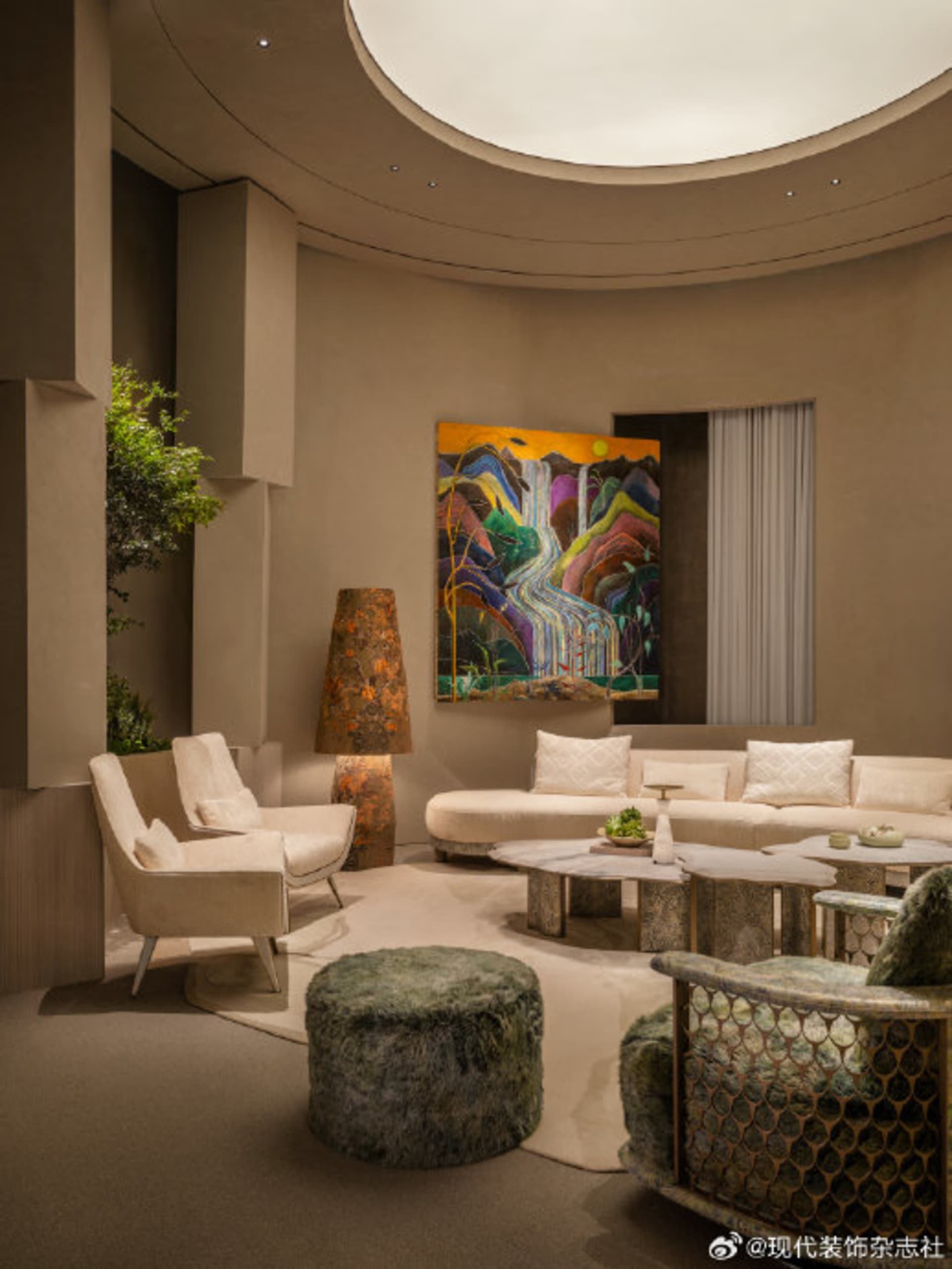 Modern curved living room featuring a creamy white curved sofa, travertine coffee tables, a green fur ottoman, and a large colorful abstract landscape painting on a curved beige wall.