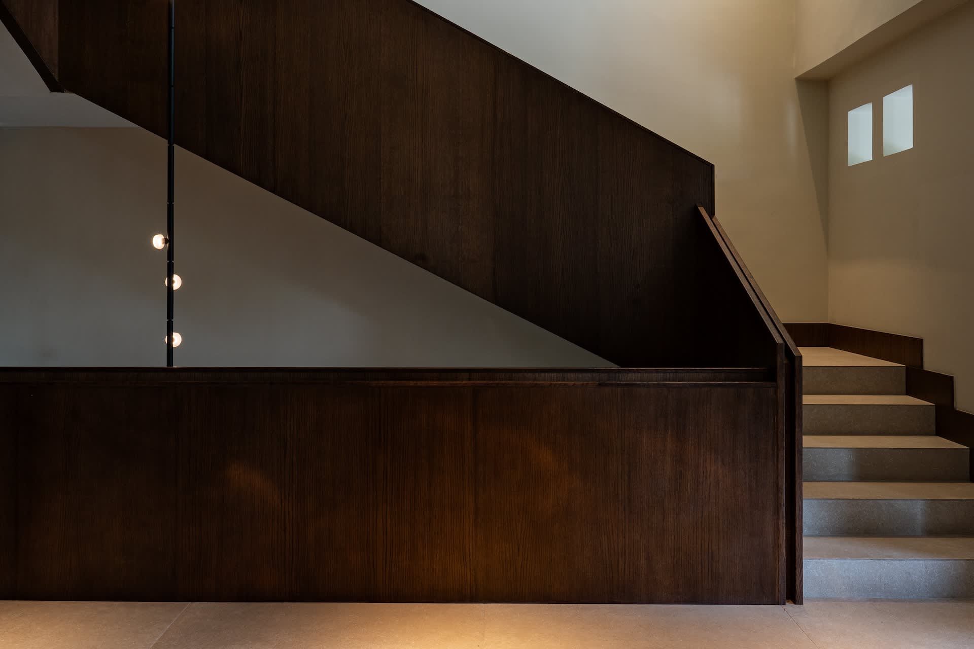 Modern minimalist interior featuring a dark walnut wood staircase with vertical pendant lighting and concrete steps.