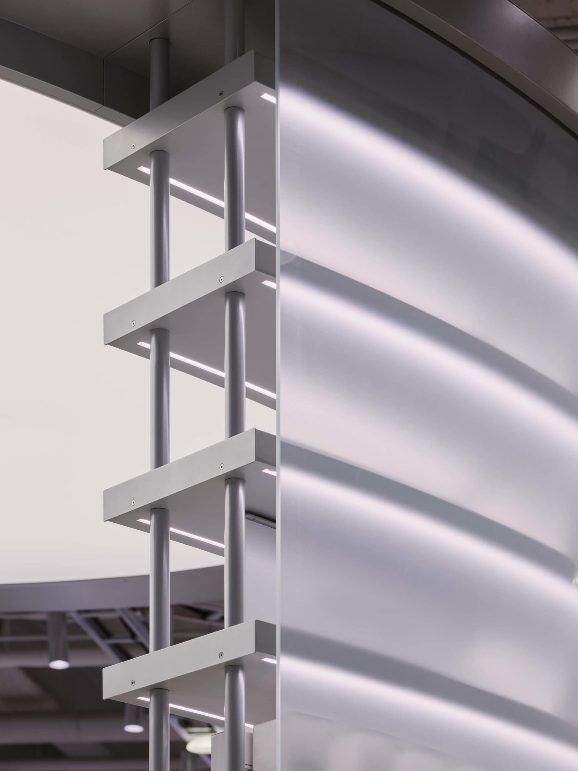 Close-up view of a modern architectural glass partition featuring a white anodized aluminum frame with integrated linear LED lighting and cylindrical supports.