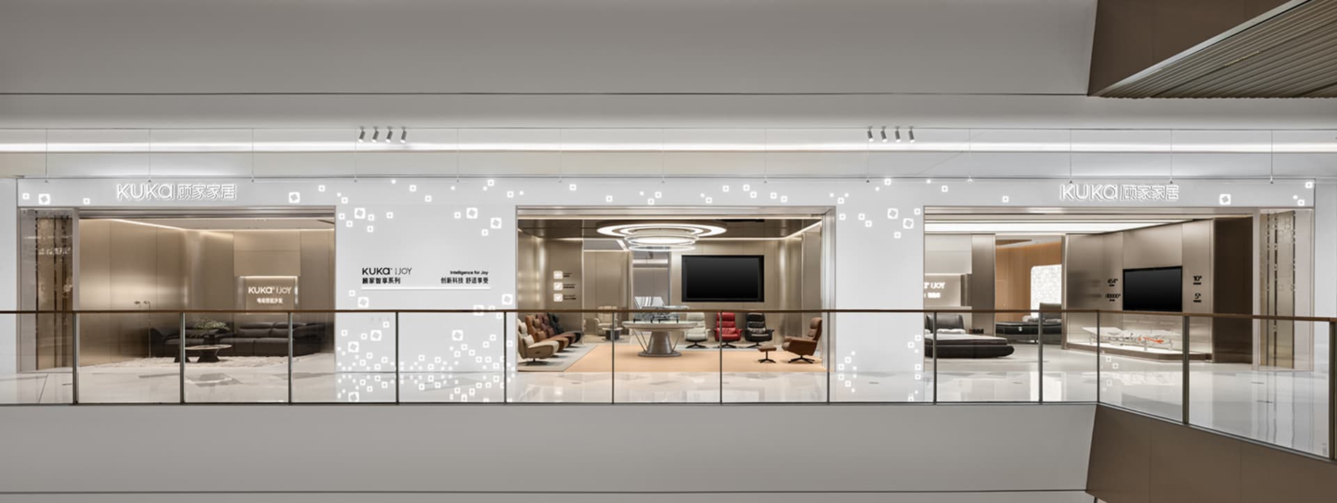 Wide view of the KUKA Joy smart furniture showroom on an upper retail level, showcasing multiple modern living room vignettes behind glass railings with illuminated branding.
