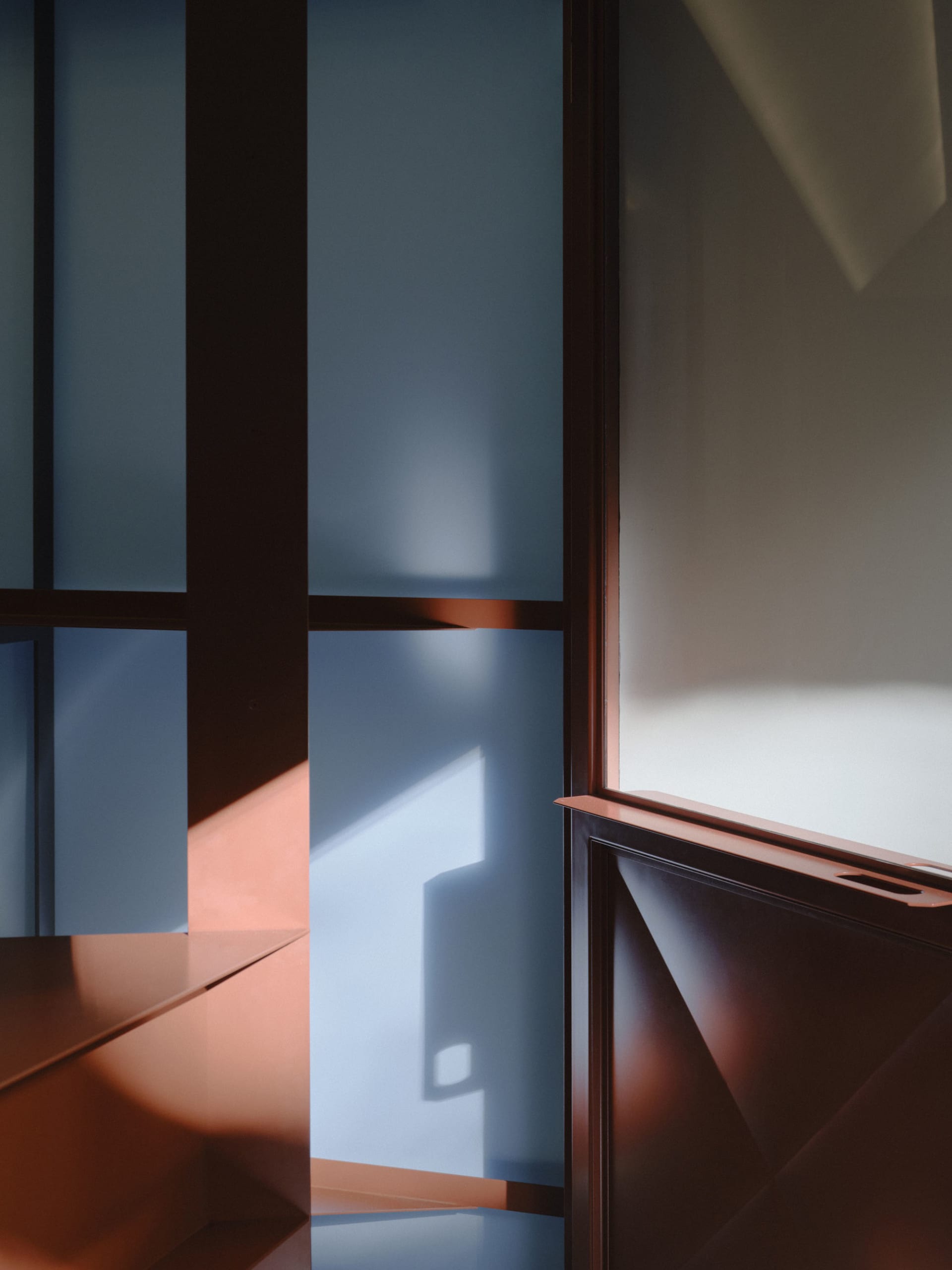 Close-up architectural detail of dark walnut wood panels and shelves with strong morning sunlight casting blue and warm orange shadows on the walls.