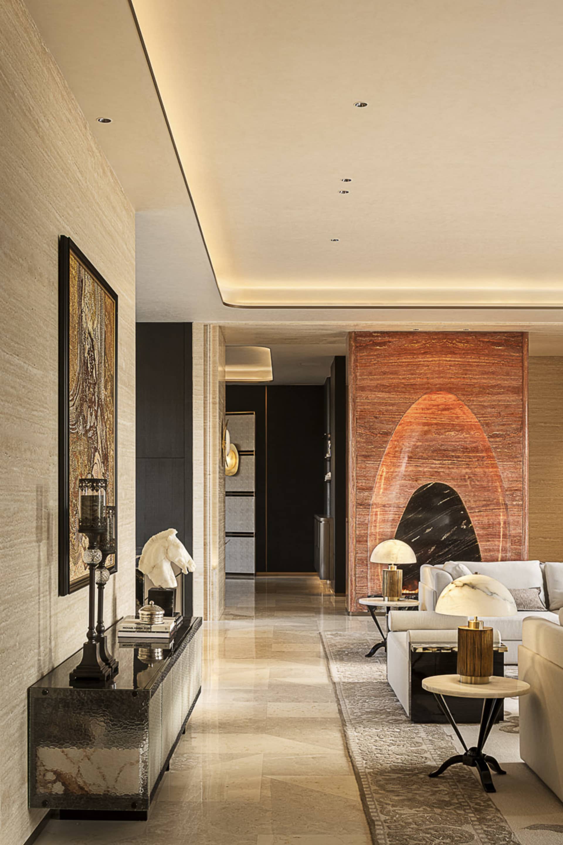 Modern luxury living room hallway featuring a dark marble console table, horse head sculpture, framed artwork, and a striking red onyx feature wall in the background with white sofas.