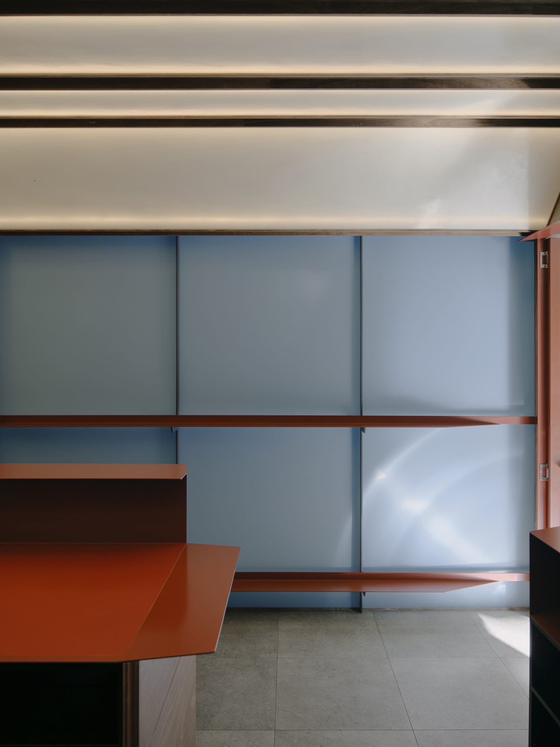 Modern interior featuring a terracotta-colored storage unit and large blue cabinet doors with integrated lighting and concrete flooring