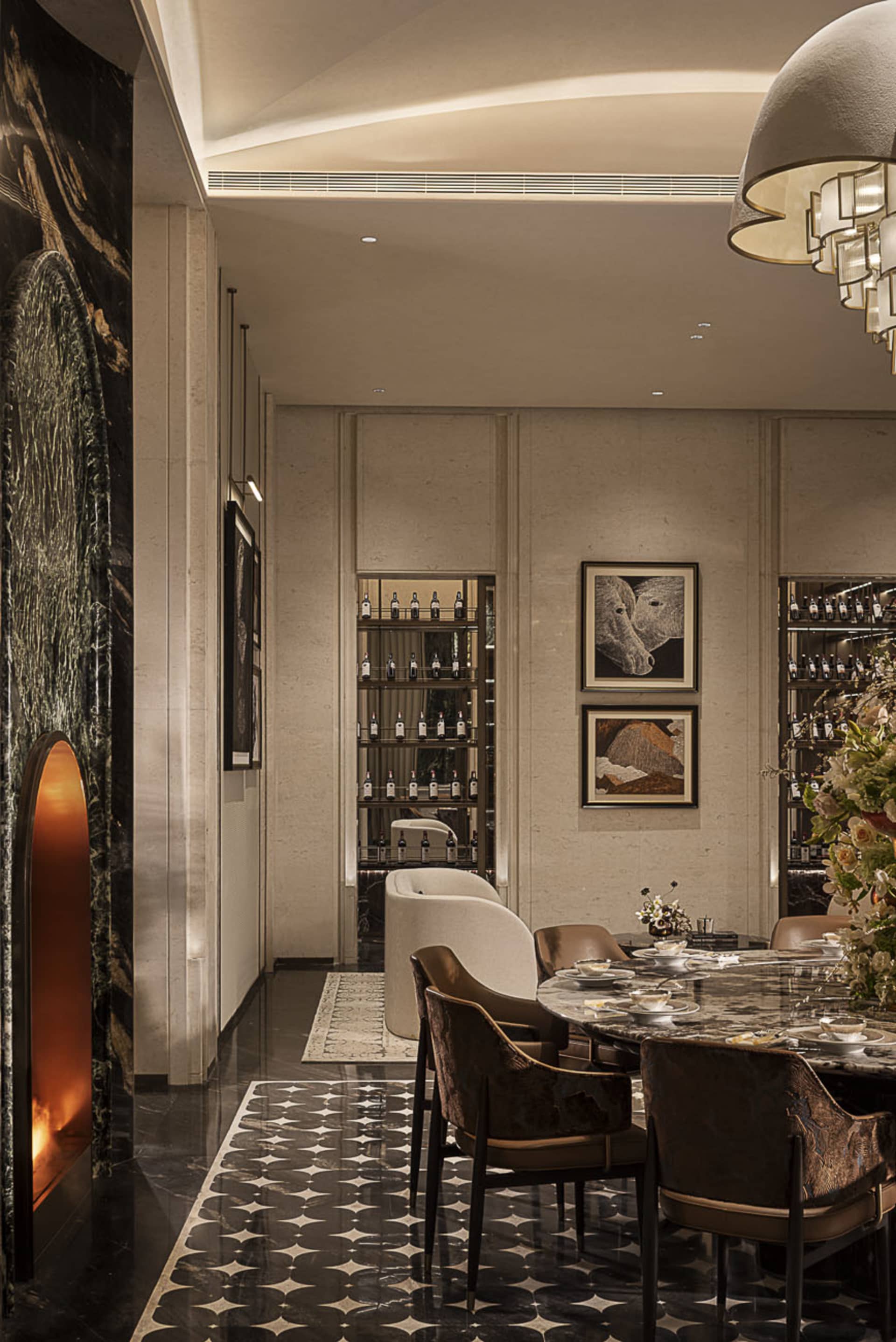 Elegant luxury dining room with dark marble fireplace, patterned black and white floor tiles, velvet dining chairs, built-in wine display, and contemporary artwork.