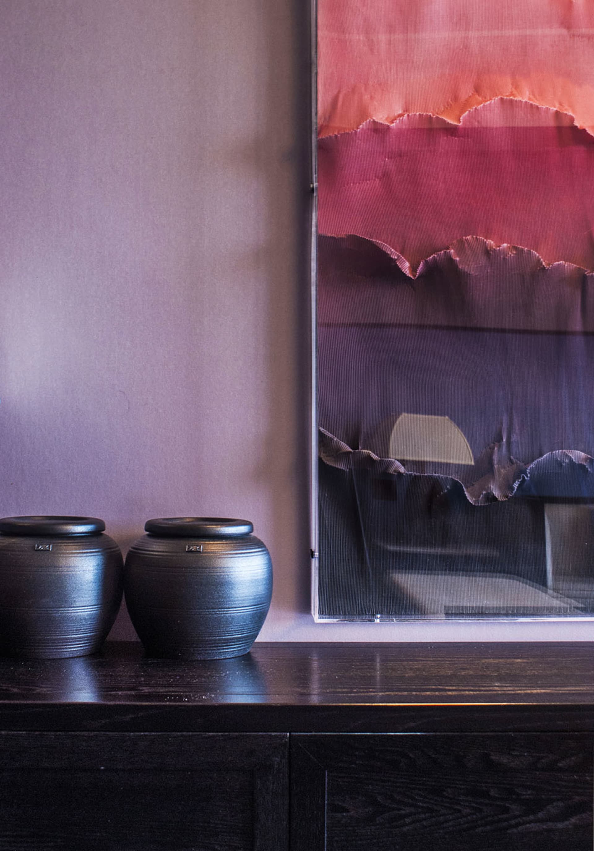 Two dark ceramic jars placed on a dark wooden console table beside a large abstract painting with red and purple tones.