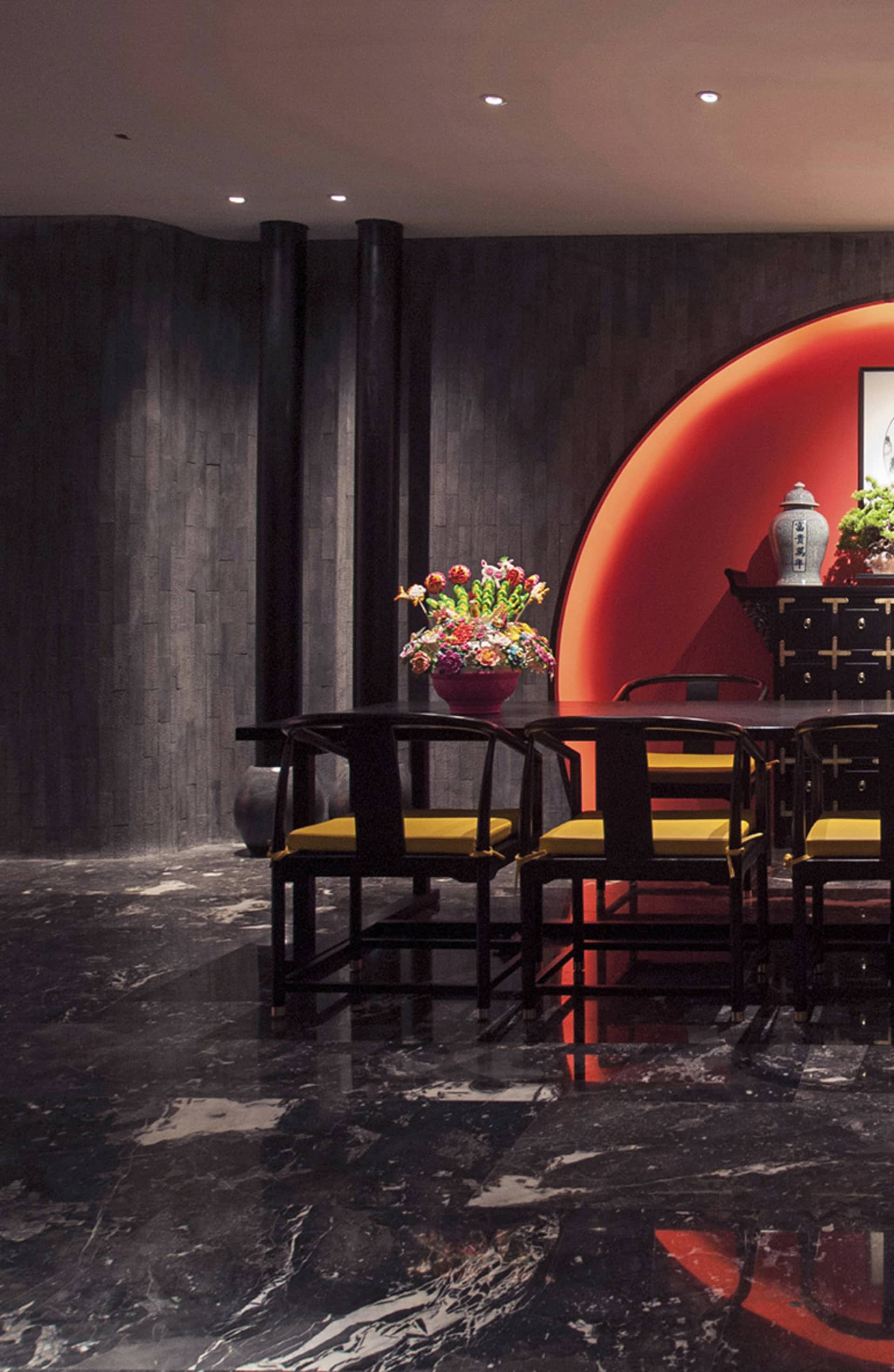 Luxurious dining room featuring dark wood Chinese-style chairs with yellow cushions, a large round red illuminated wall feature, dark marble floor, and dramatic dark wood paneling.