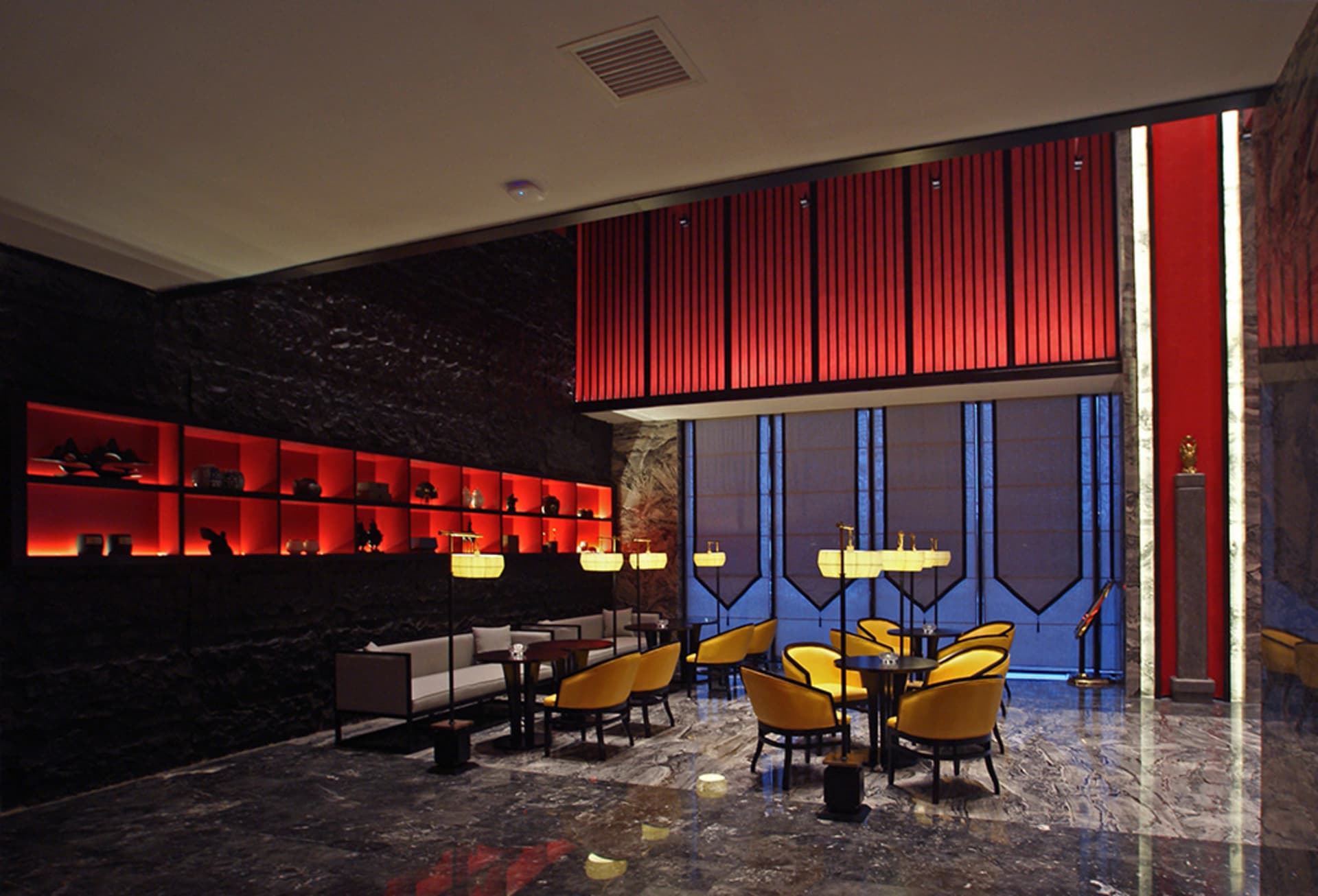 Luxury hotel lobby lounge featuring black marble walls with glowing red backlit shelves, bold red vertical slat feature wall, polished marble floor, and golden yellow velvet armchairs arranged in intimate seating groups.