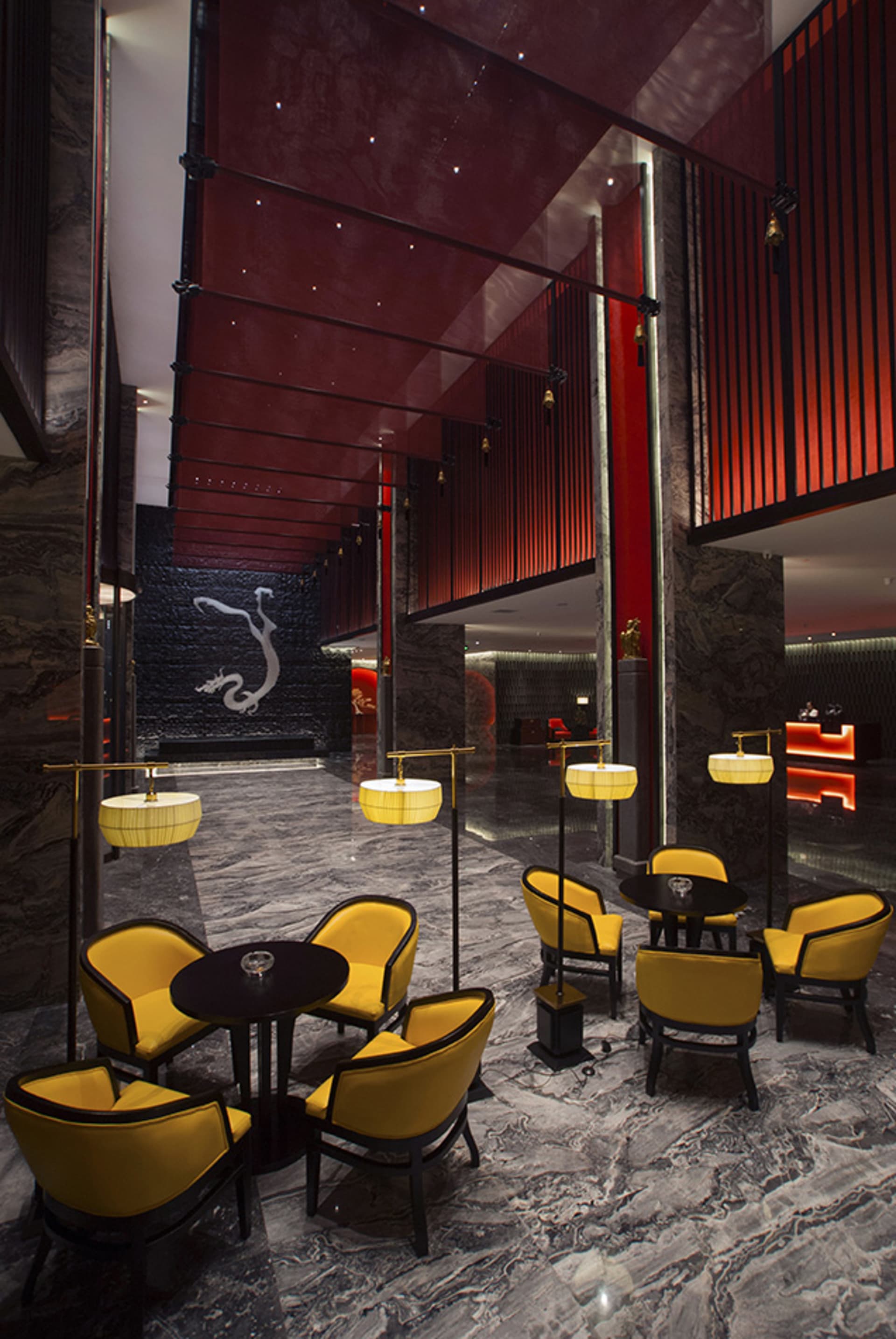 Luxurious hotel lobby featuring grey marble floors, yellow velvet armchairs, black tables, dramatic red ceiling panels, and a large white dragon mural on a black stone wall.