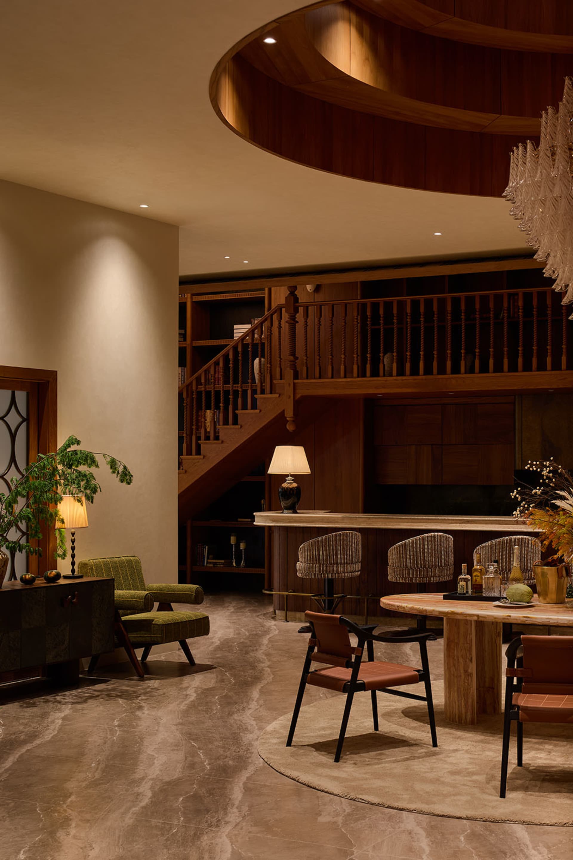Luxurious double-height living and dining area featuring a dramatic curved walnut wood ceiling, marble floor, green patterned armchair, leather dining chairs, and a grand crystal chandelier.