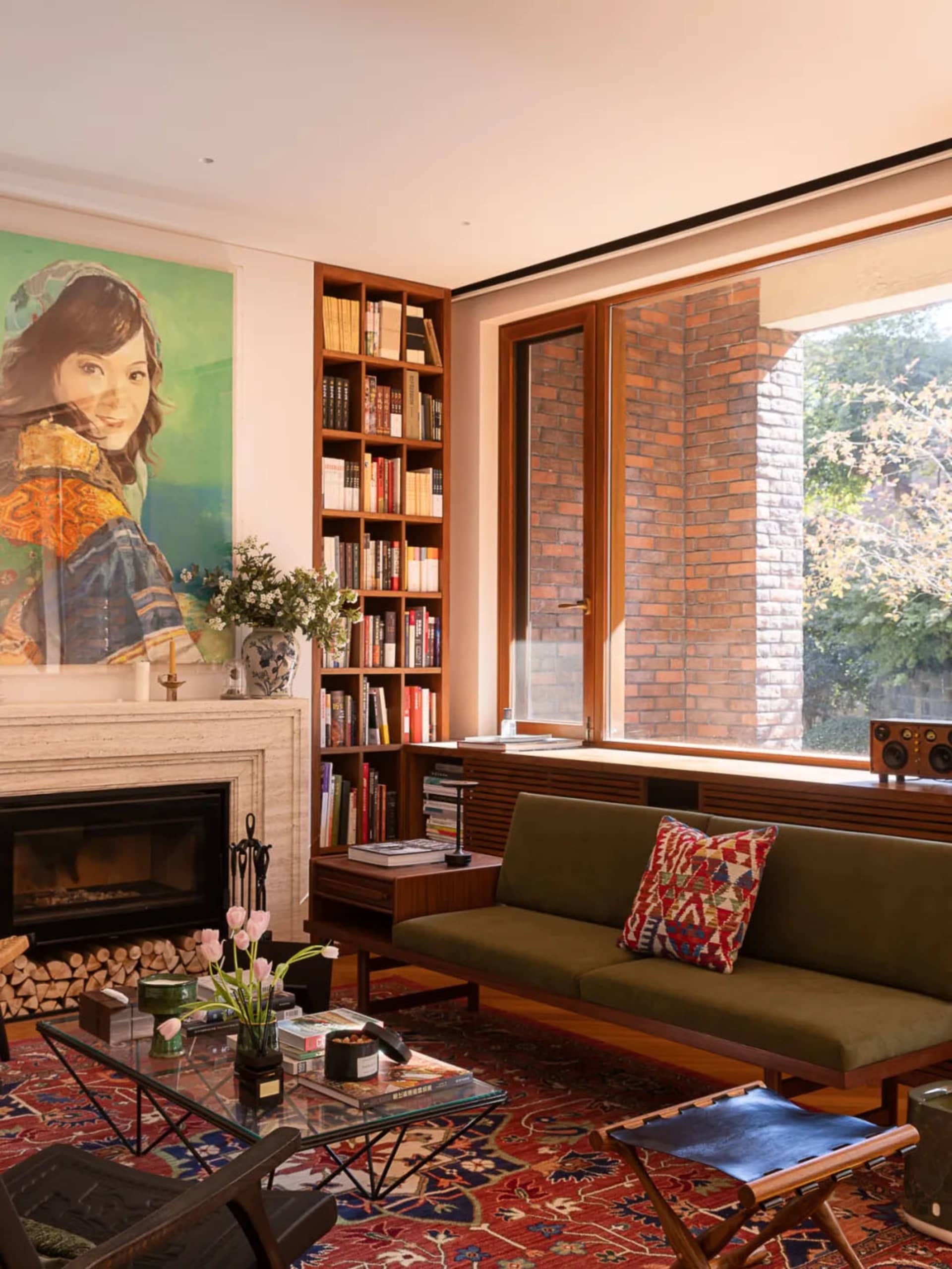 Cozy living room with olive green sofa, walnut bookshelf, brick wall, marble fireplace, and large colorful portrait painting