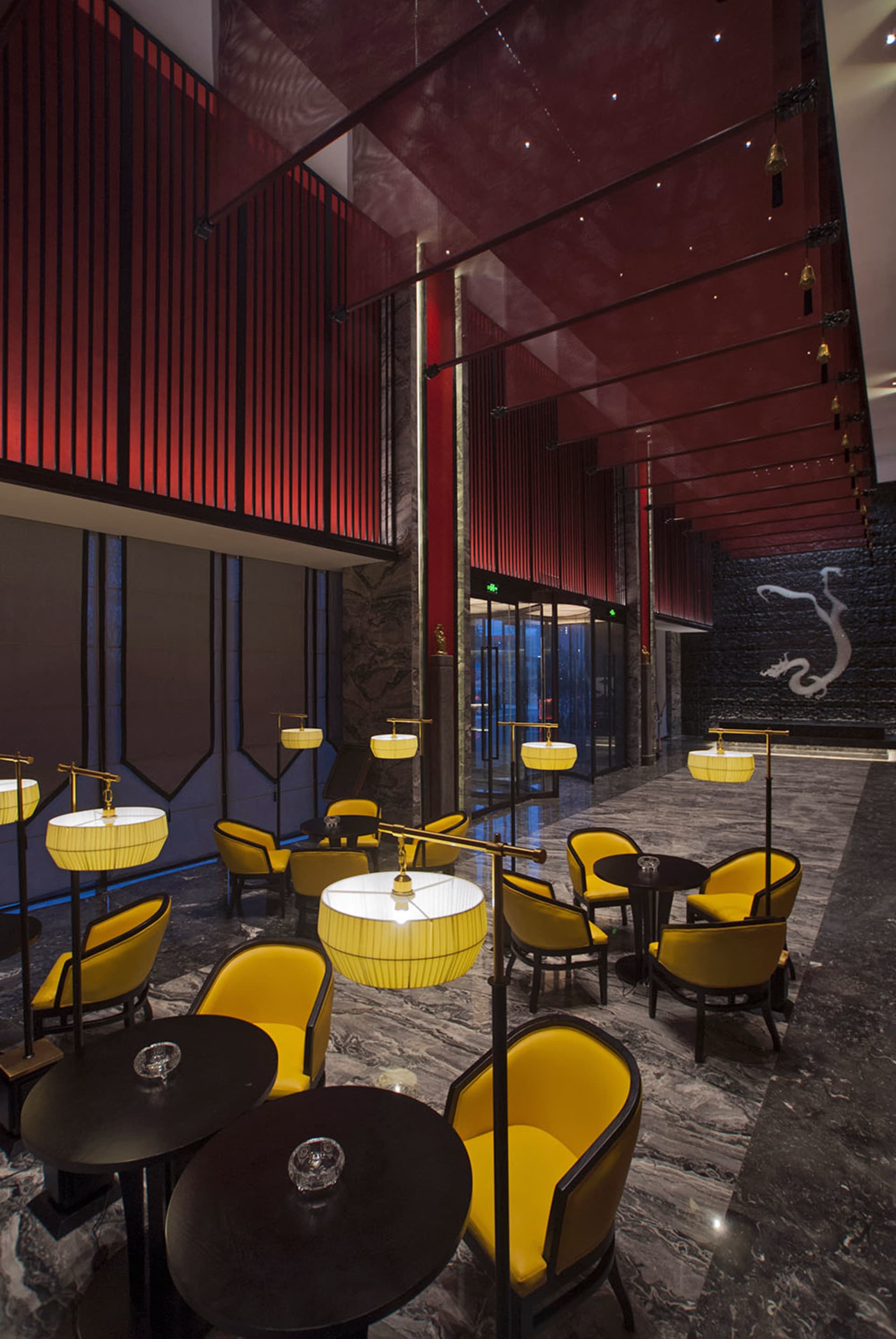 奢華飯店大廳休憩區，設有鮮黃色絨布扶手椅、黑色圓桌、戲劇感的紅色垂直板條牆，以及灰色大理石地板，背景有大型白色龍形壁畫。