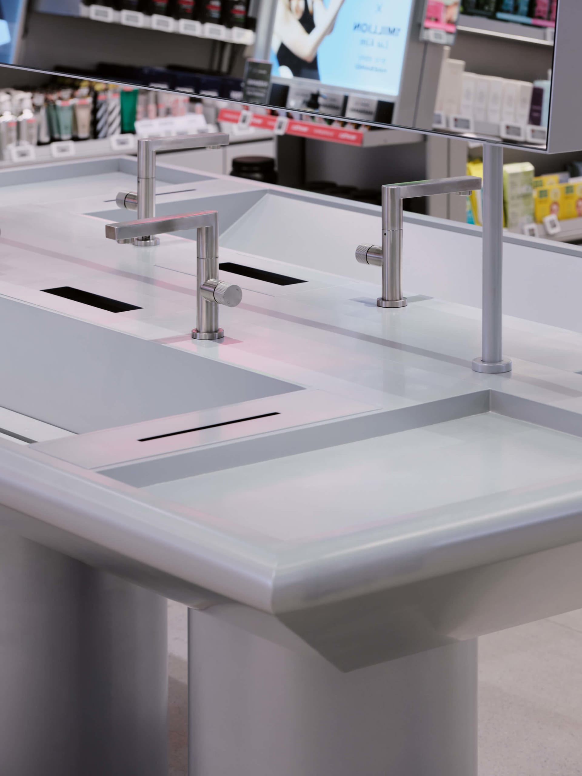 Modern white bathroom vanity counter with integrated rectangular sinks and brushed stainless steel faucets in a showroom setting.