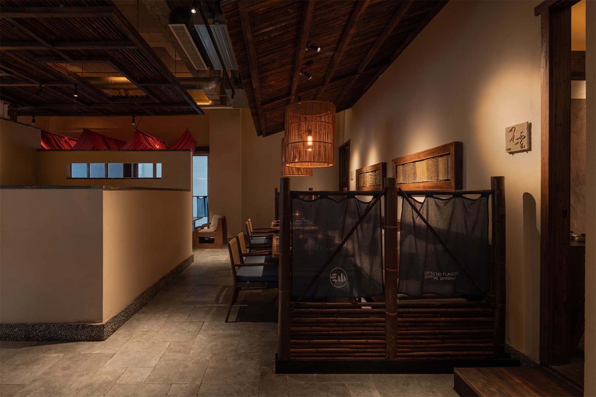 Interior view of a Japanese restaurant featuring bamboo partitions, wooden beams, woven rattan lanterns, and warm earthy tones.