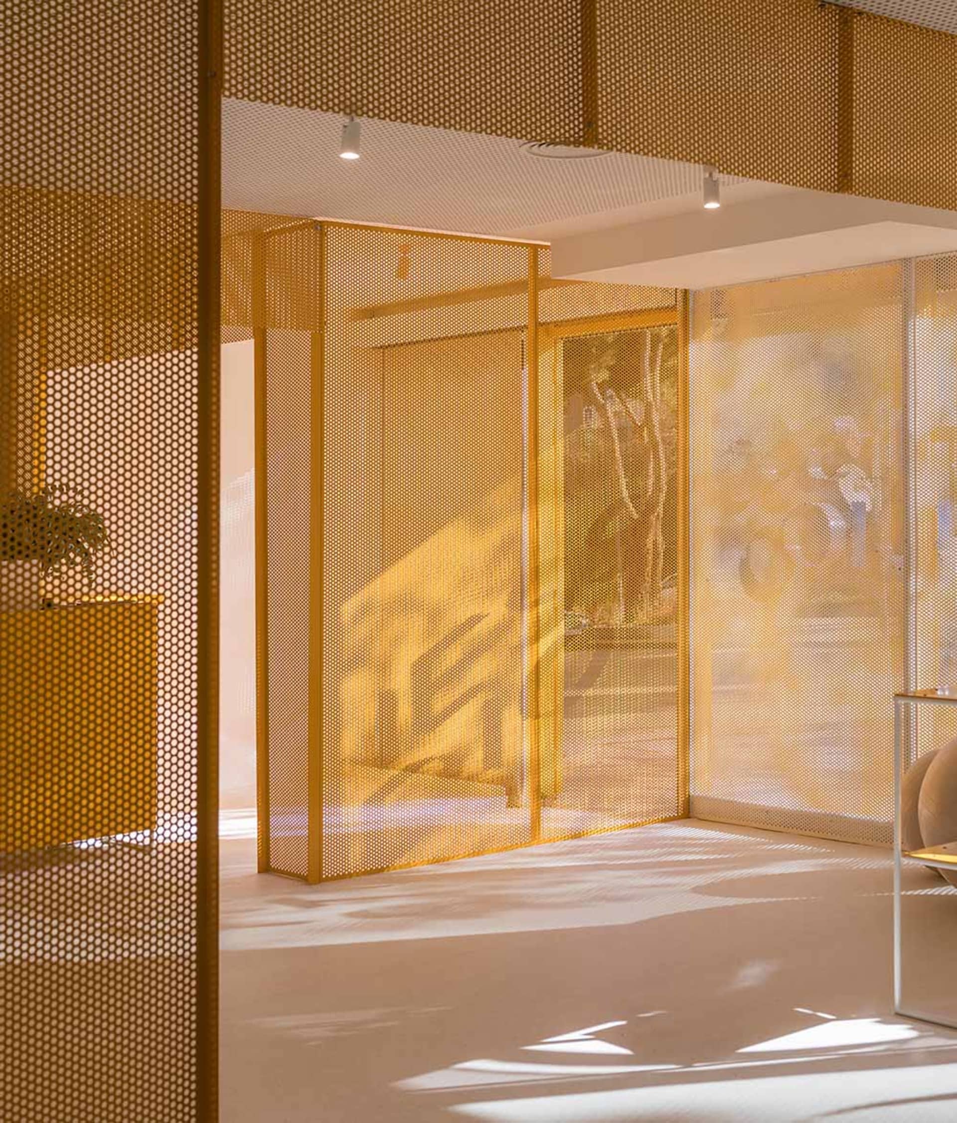 Modern commercial interior featuring golden perforated brass room dividers with dramatic light and shadow patterns on the floor.