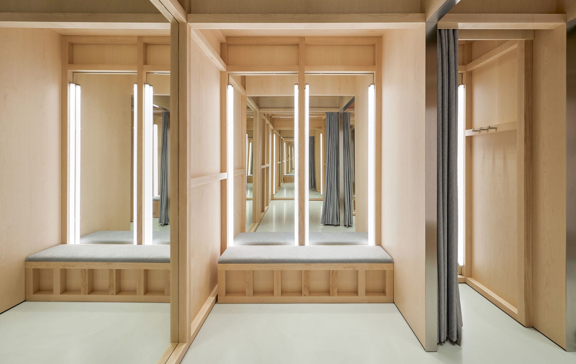 Modern Japanese style entryway with light wood cabinetry, grey upholstered built-in benches, vertical LED light bars, and multiple mirrors creating an infinite reflection hallway effect.