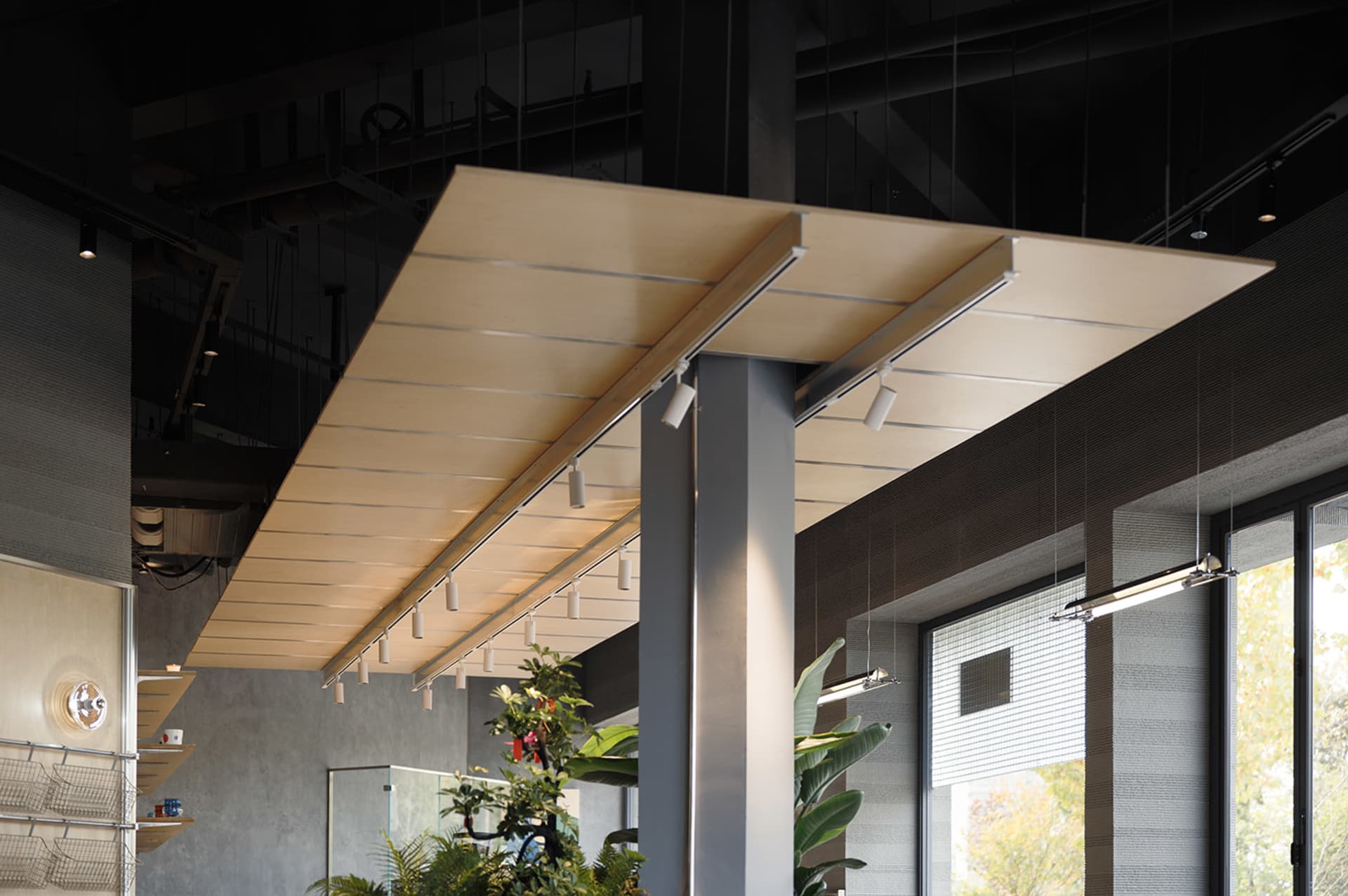 Modern industrial interior featuring a large suspended plywood ceiling canopy with integrated linear track lighting, concrete walls, and indoor plants.