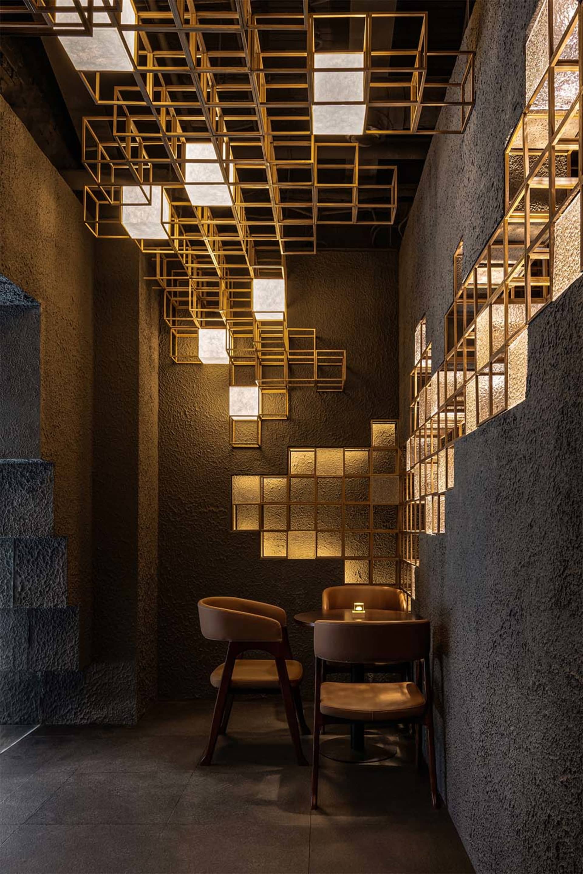現代餐廳用餐角落,特色為粗糙灰泥牆面、皮革座椅,以及懸掛在天花板上醒目的金色格柵燈光裝置。