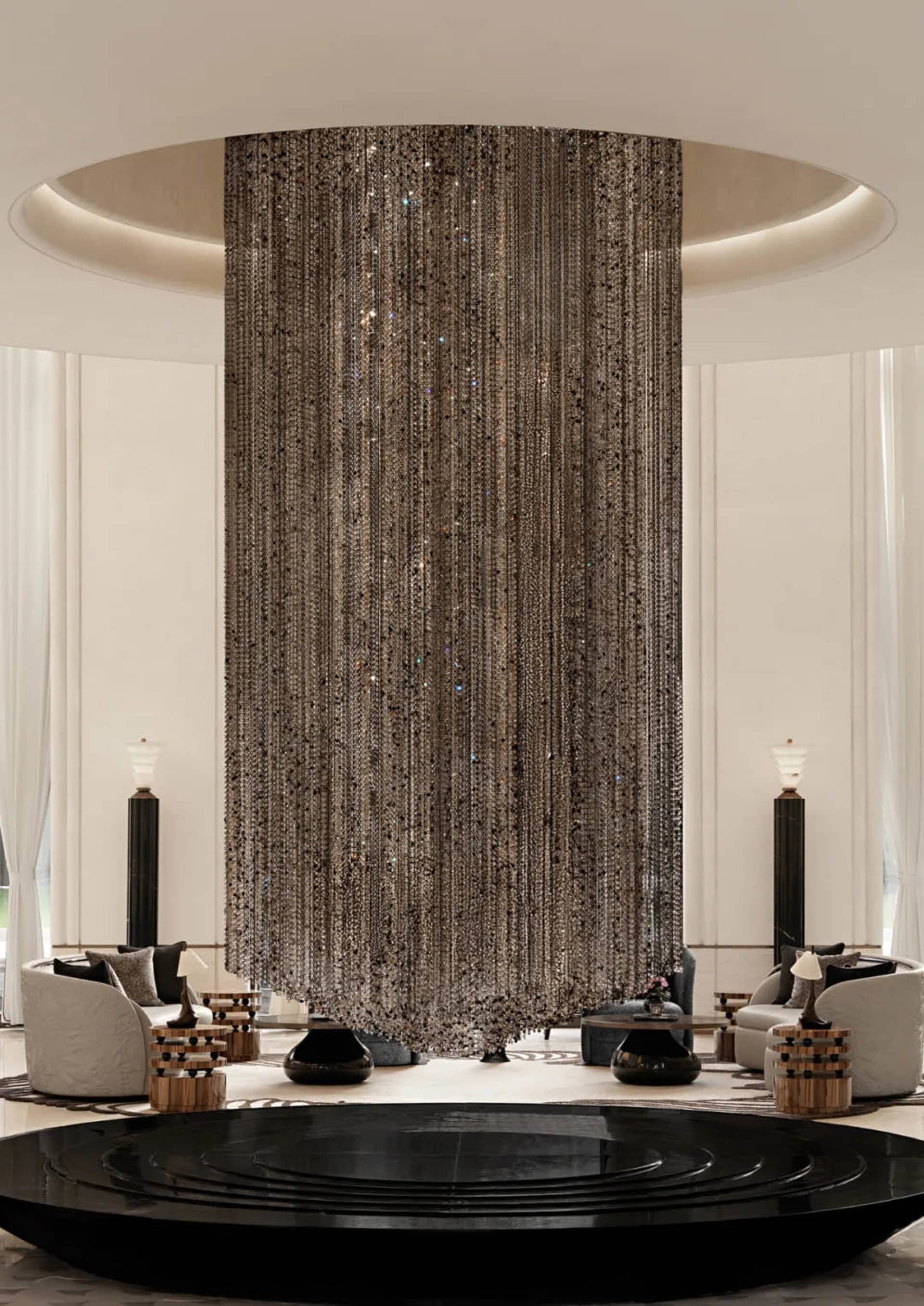 Luxurious modern lobby featuring a massive sparkling crystal bead curtain hanging from a circular ceiling, surrounded by white curved sofas and black sculptural coffee tables on a light marble floor.