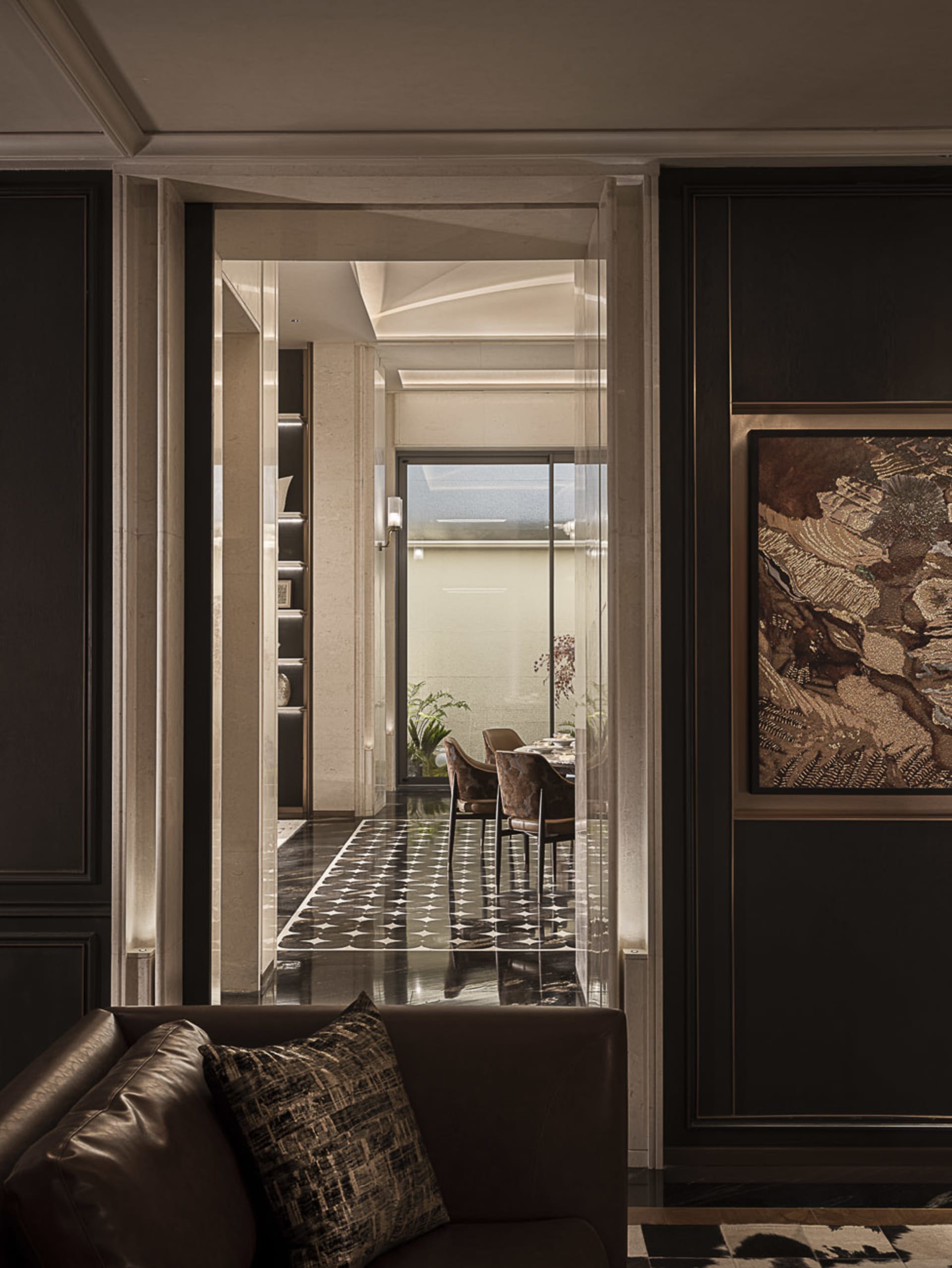 View from a dark brown leather sofa into a luxurious dining room with black and white patterned marble floor, velvet dining chairs, and large abstract artwork.