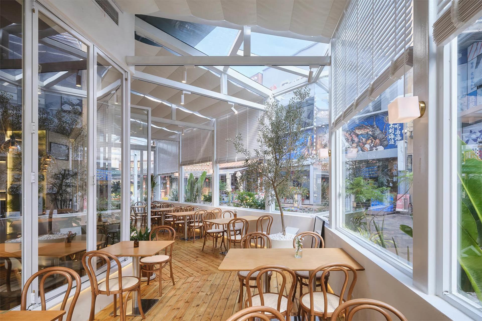 Modern glasshouse-style restaurant interior with wooden tables, bentwood chairs, skylight ceiling and large windows overlooking the street.